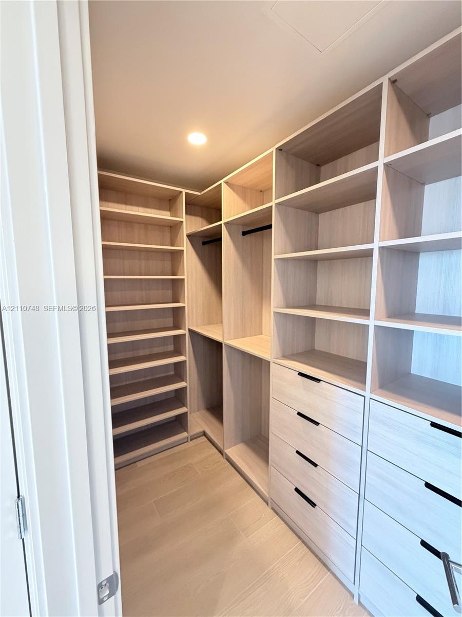 Custom walk-in closet featuring light-toned wood-finish cabinetry, floor-to-ceiling shelving, recessed lighting, and integrated drawers with matte bla