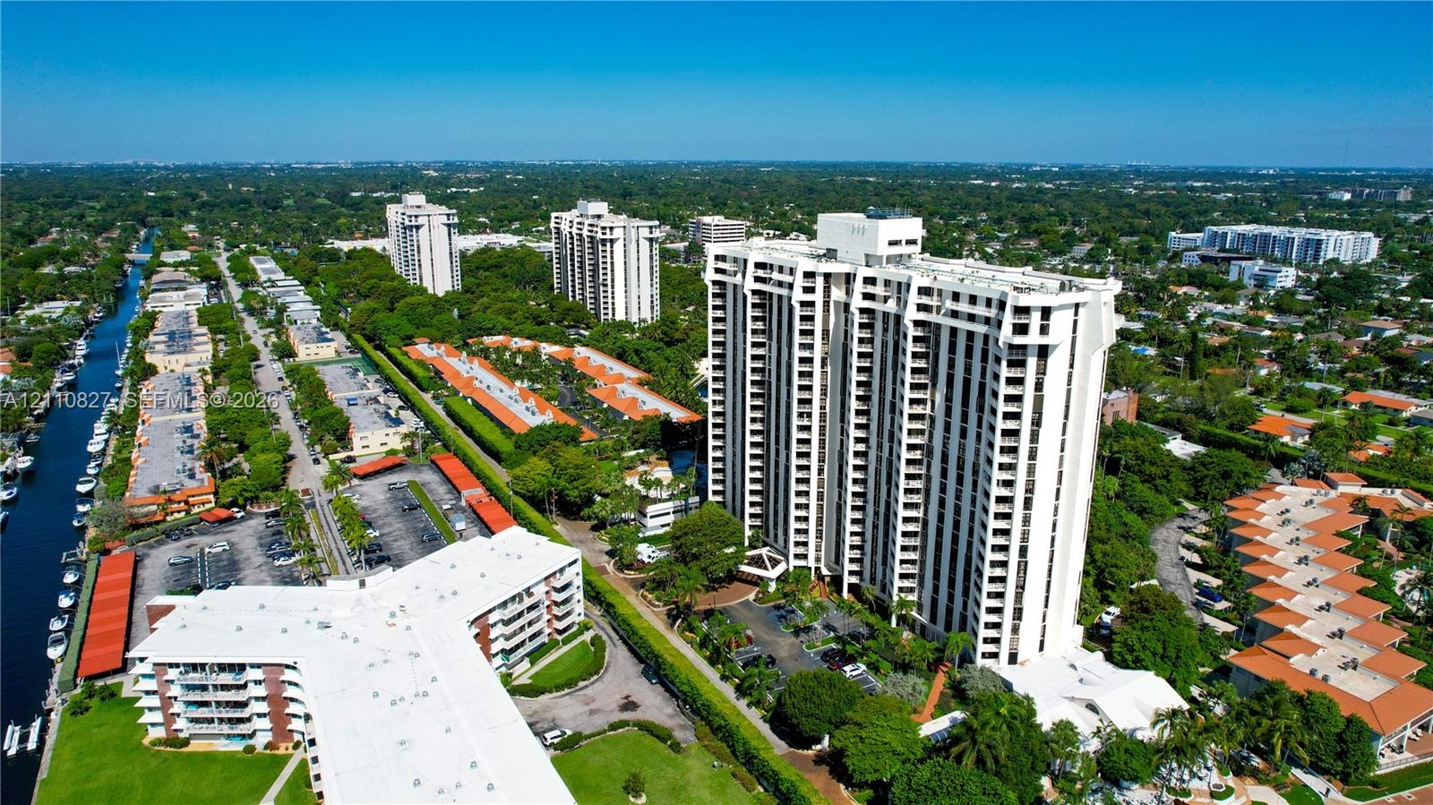 Aerial perspective of a high-rise residential structure featuring tiered balconies, covered parking areas, manicured grounds, and immediate access to 