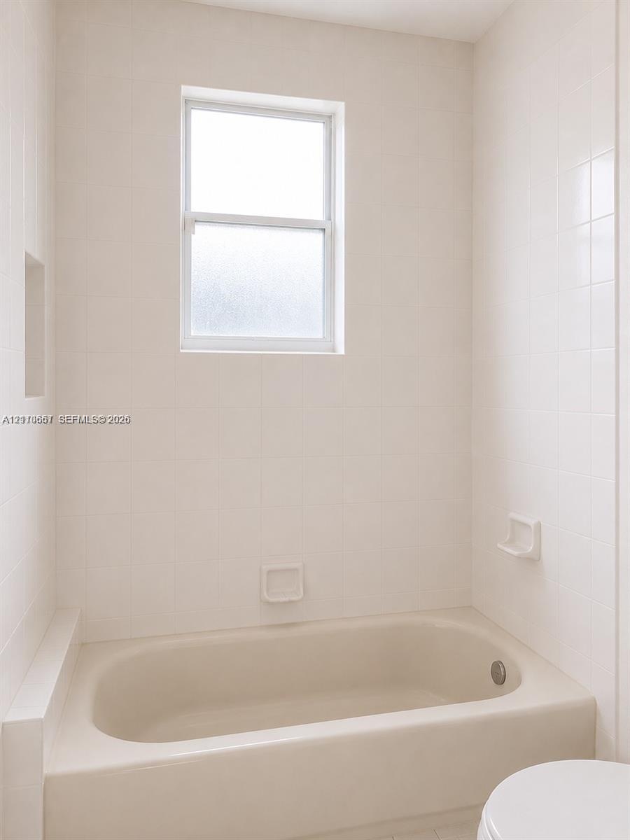 Bathtub with a shower surround featuring white tile wall cladding, an inset soap niche, and a single-hung window