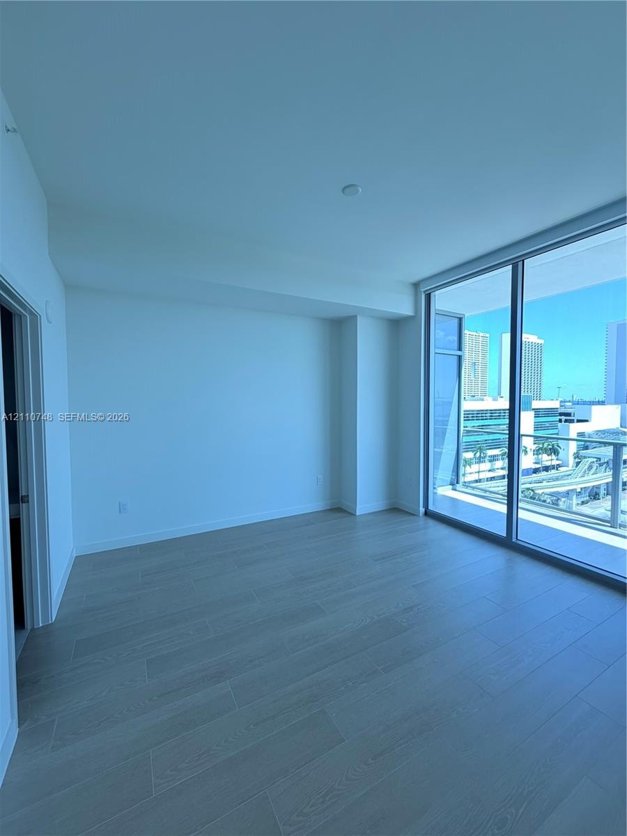 Floor-to-ceiling glass sliding doors, wood-finish flooring, and a private balcony with metallic railing