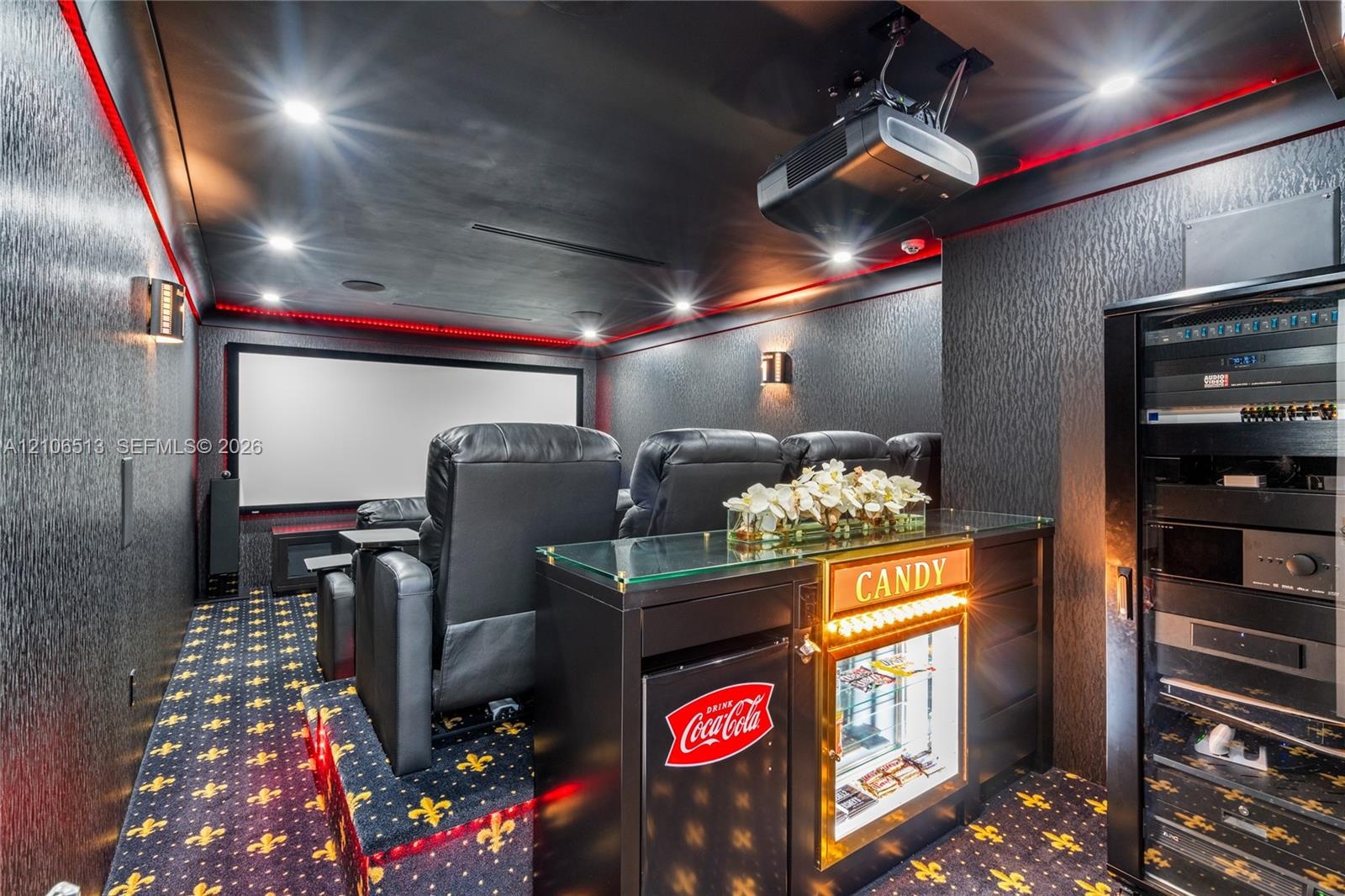 Dedicated media room featuring a large projection screen, recessed lighting, integrated ceiling-mounted projection equipment, and a built-in equipment