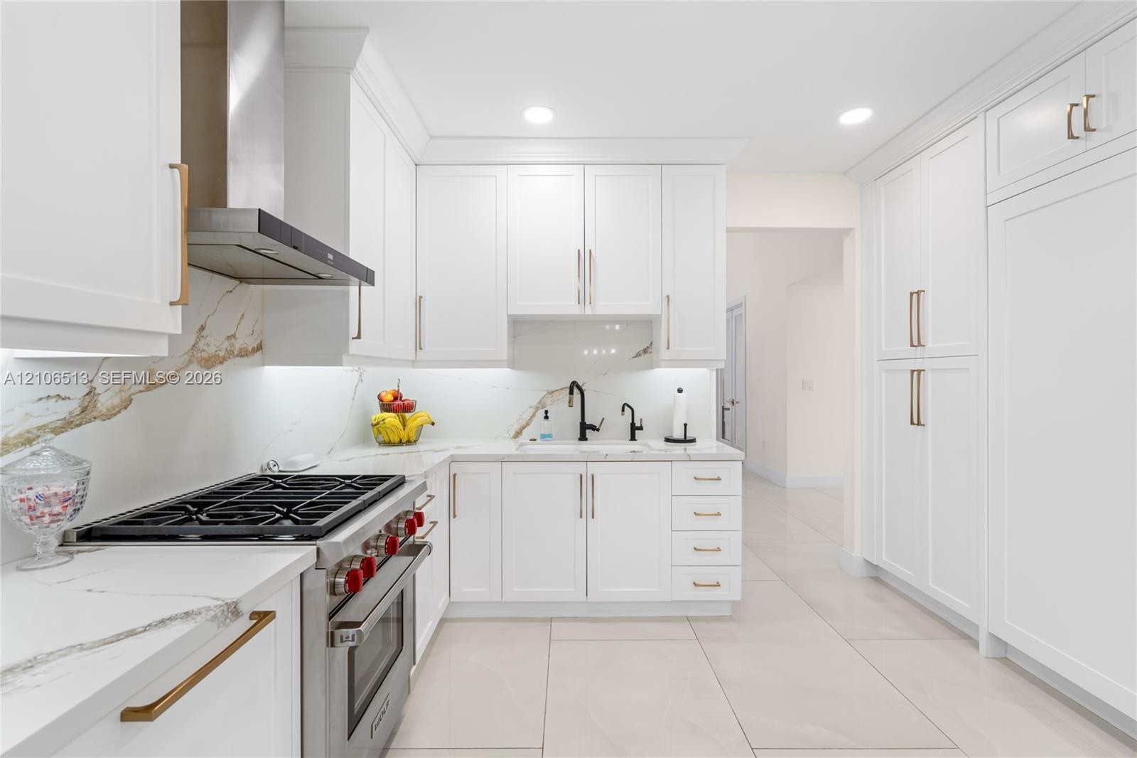 Kitchen featuring shaker-style white cabinetry, stone-finish countertops with matching full-height backsplash, stainless steel gas range with overhead