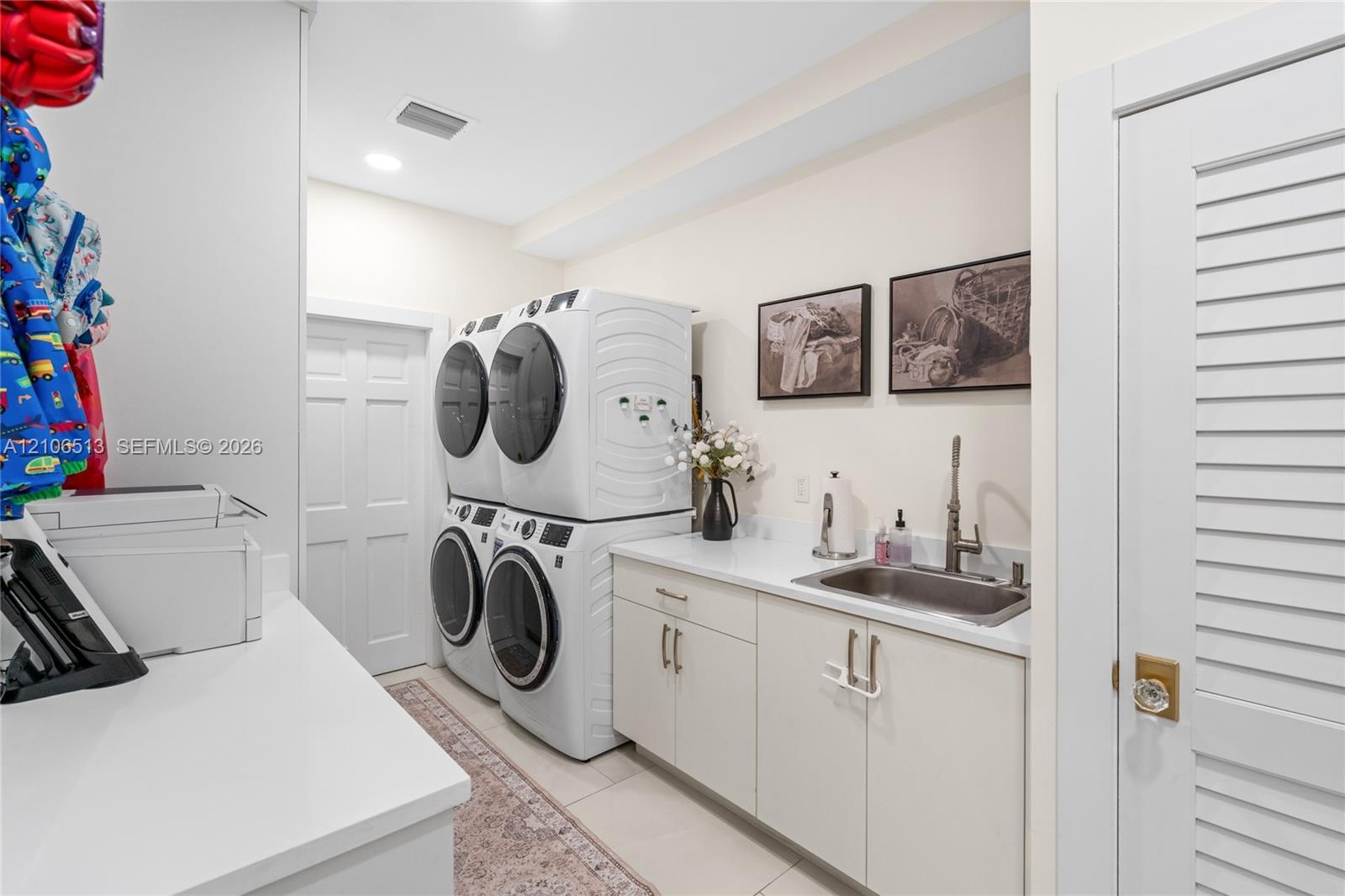 Laundry room featuring stacked washer and dryer units, solid-surface countertops, an undermount stainless steel sink with a high-arch faucet, custom f