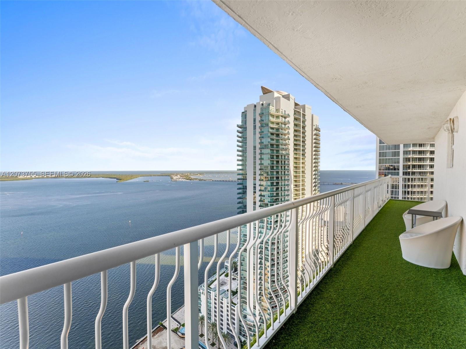 Private balcony featuring a synthetic turf floor, white metal railing, and extensive water and city skyline surroundings