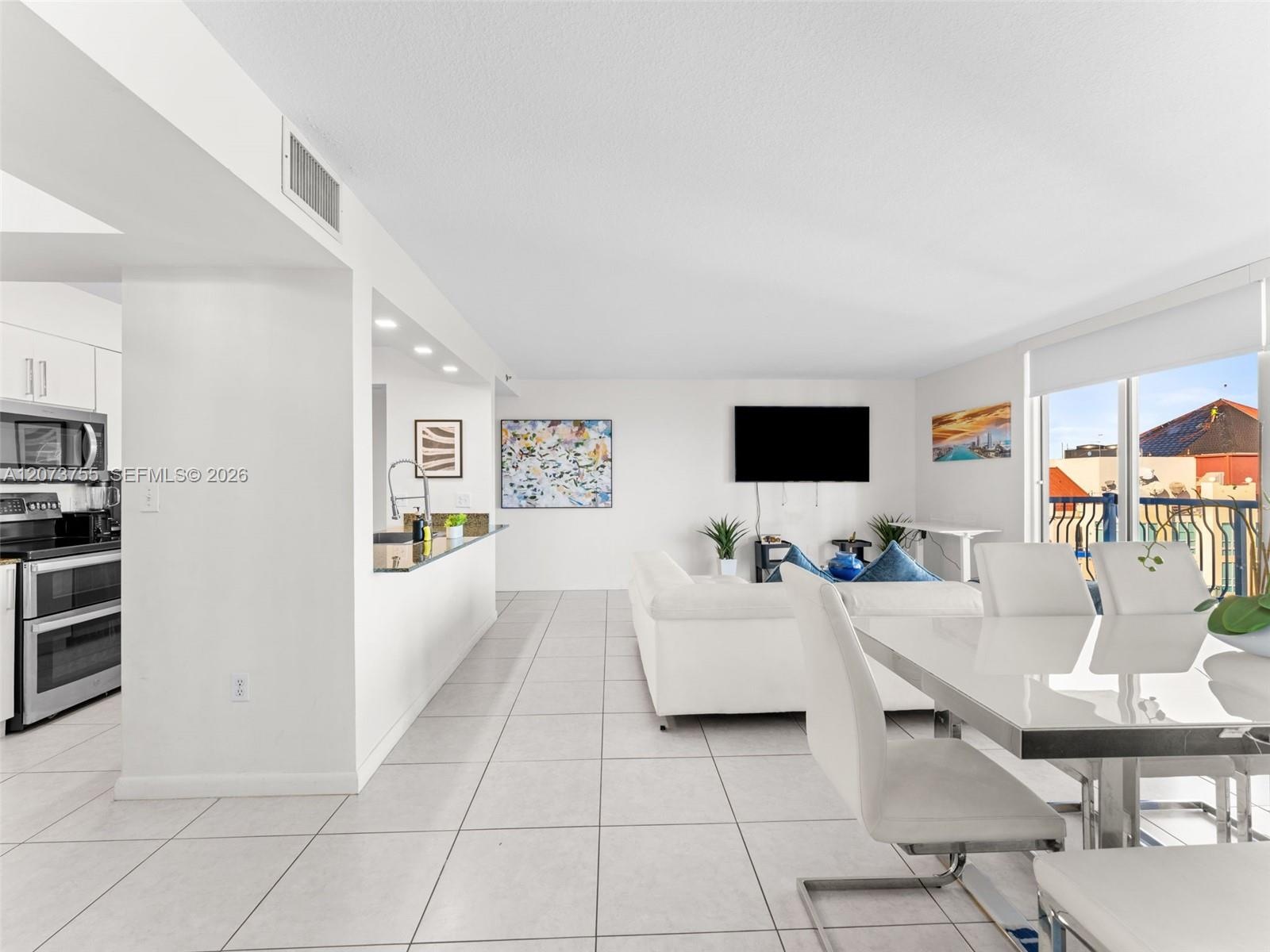 Open-concept interior featuring white floor tiling, a pass-through kitchen counter with stone-finish surfacing, stainless steel appliances, and a larg