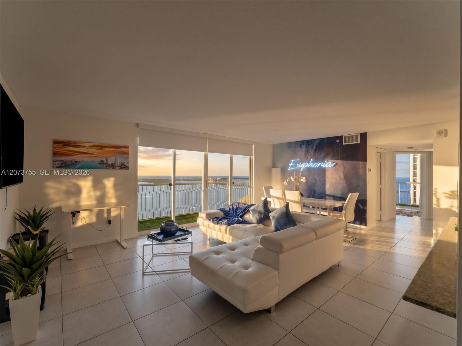 Open-concept living area featuring large-format ceramic tile flooring, floor-to-ceiling glass sliding doors, and a private balcony