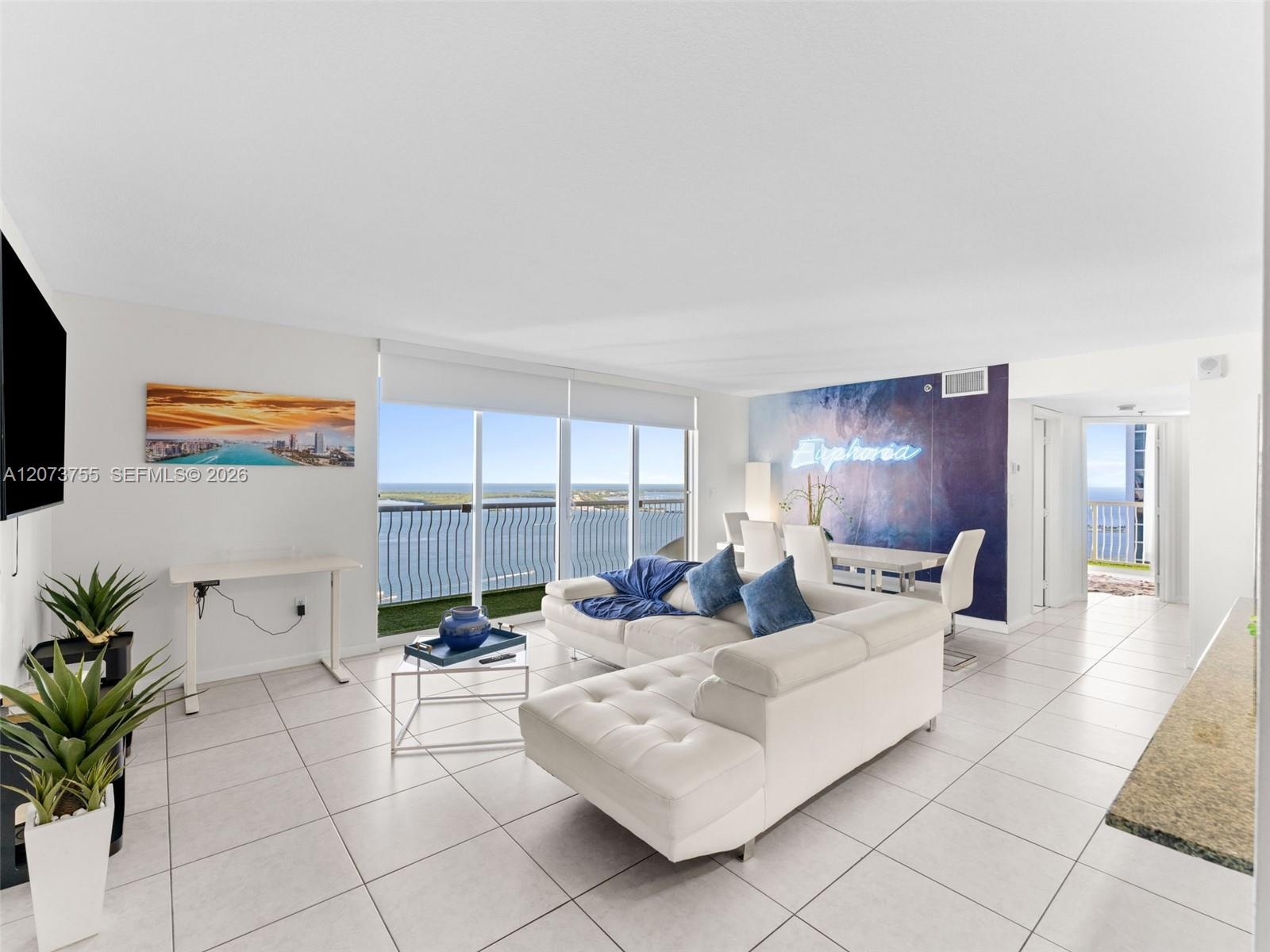 Living area featuring floor-to-ceiling glass sliding doors, large-format tile flooring, a private balcony with metal railing, and a distinctive accent