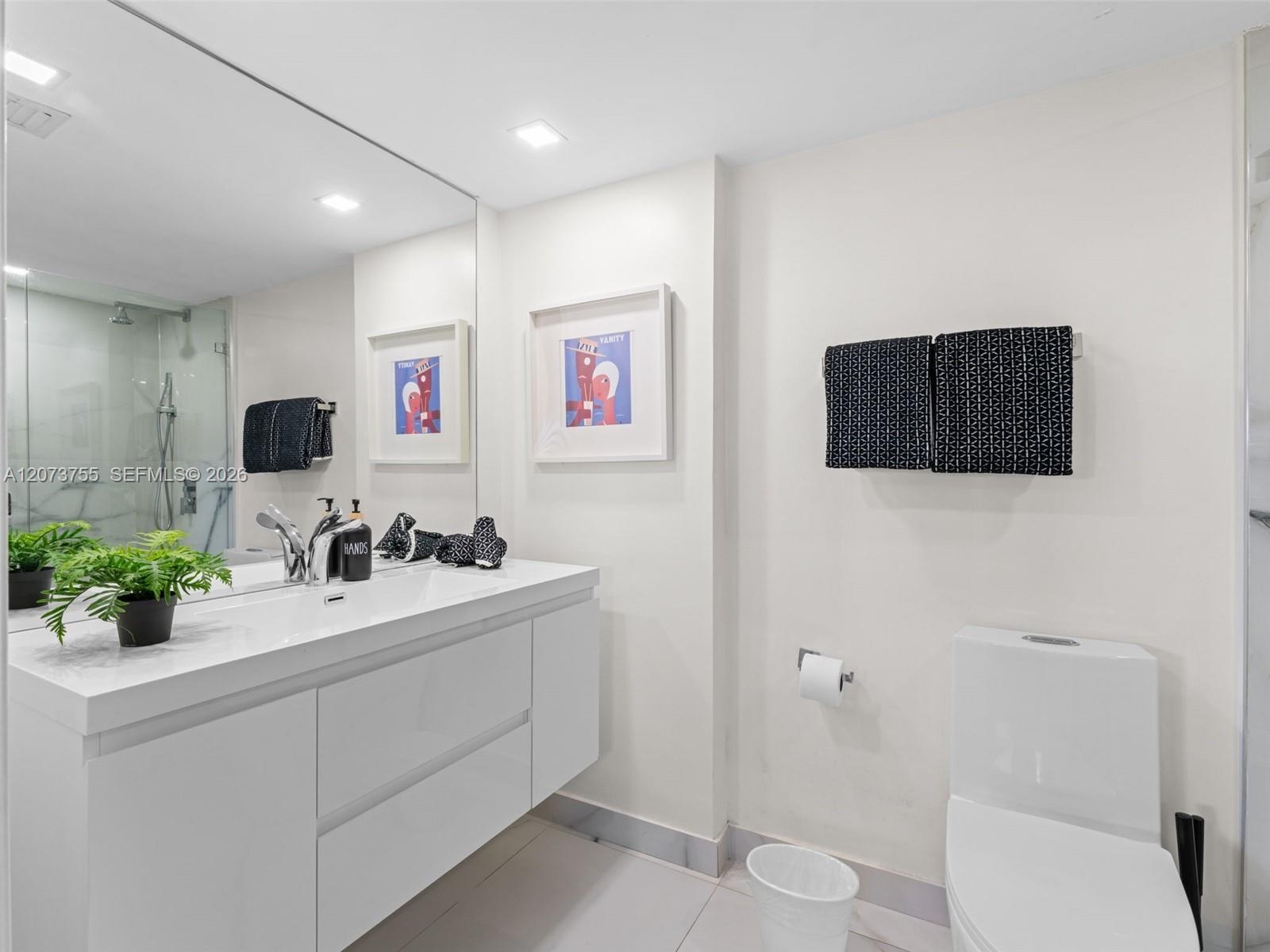 Floating vanity featuring a flat-panel white cabinet, integrated sink, and chrome fixtures paired with a full-width wall mirror, recessed ceiling ligh