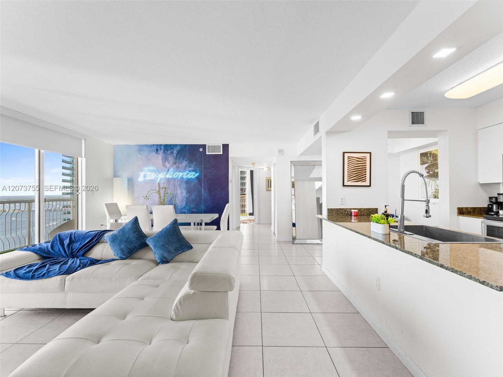 Open-concept interior featuring light-toned tile flooring, recessed ceiling lighting, kitchen island with stone countertop, stainless steel kitchen fa