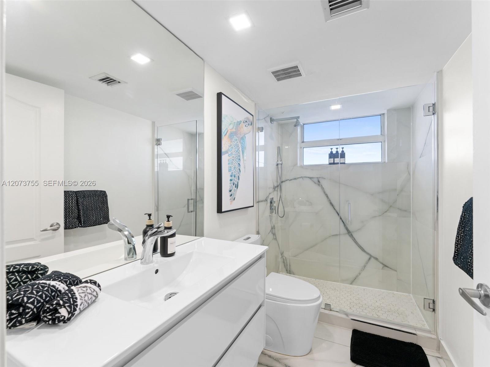 Modern floating vanity with an integrated basin, expansive wall-to-wall mirror, glass-enclosed shower with stone-vein tile surround, and recessed ceil