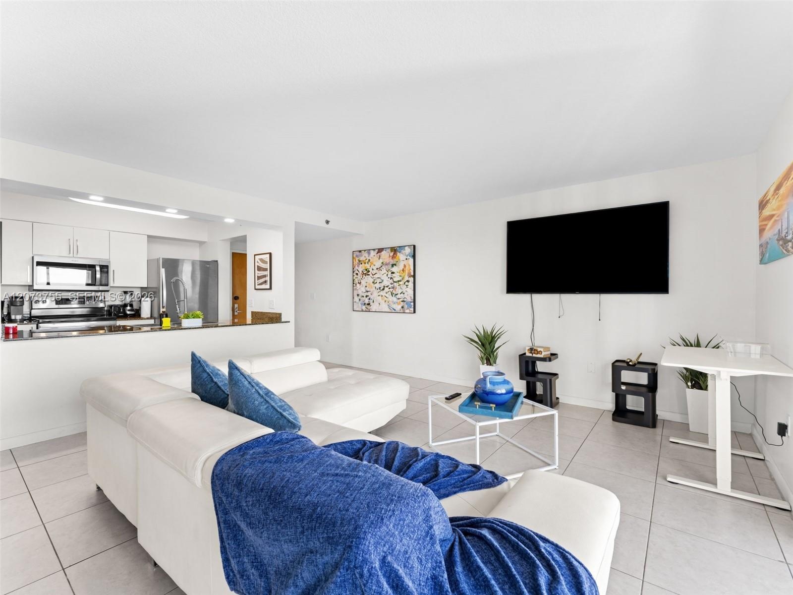 Open-concept floor plan featuring tile flooring, white cabinetry, stainless steel appliances, and a pass-through breakfast bar
