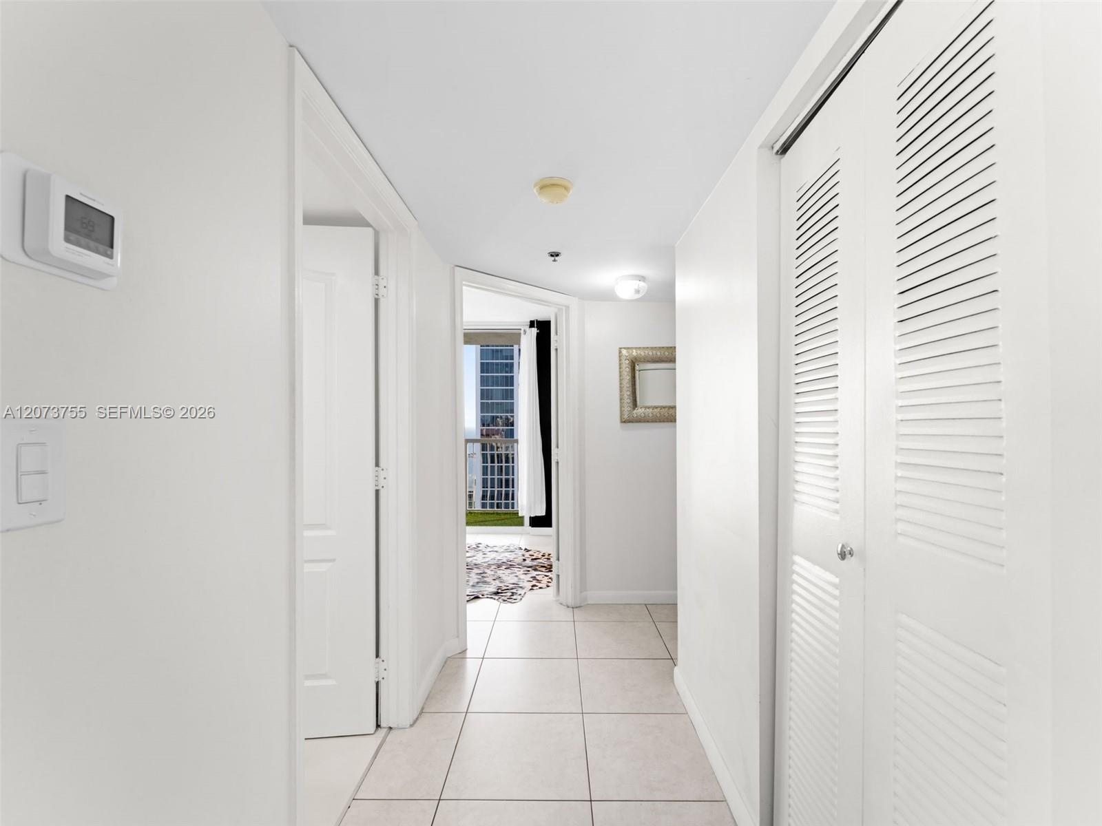 Hallway featuring tile flooring, louvered-panel closet doors, and a digital thermostat