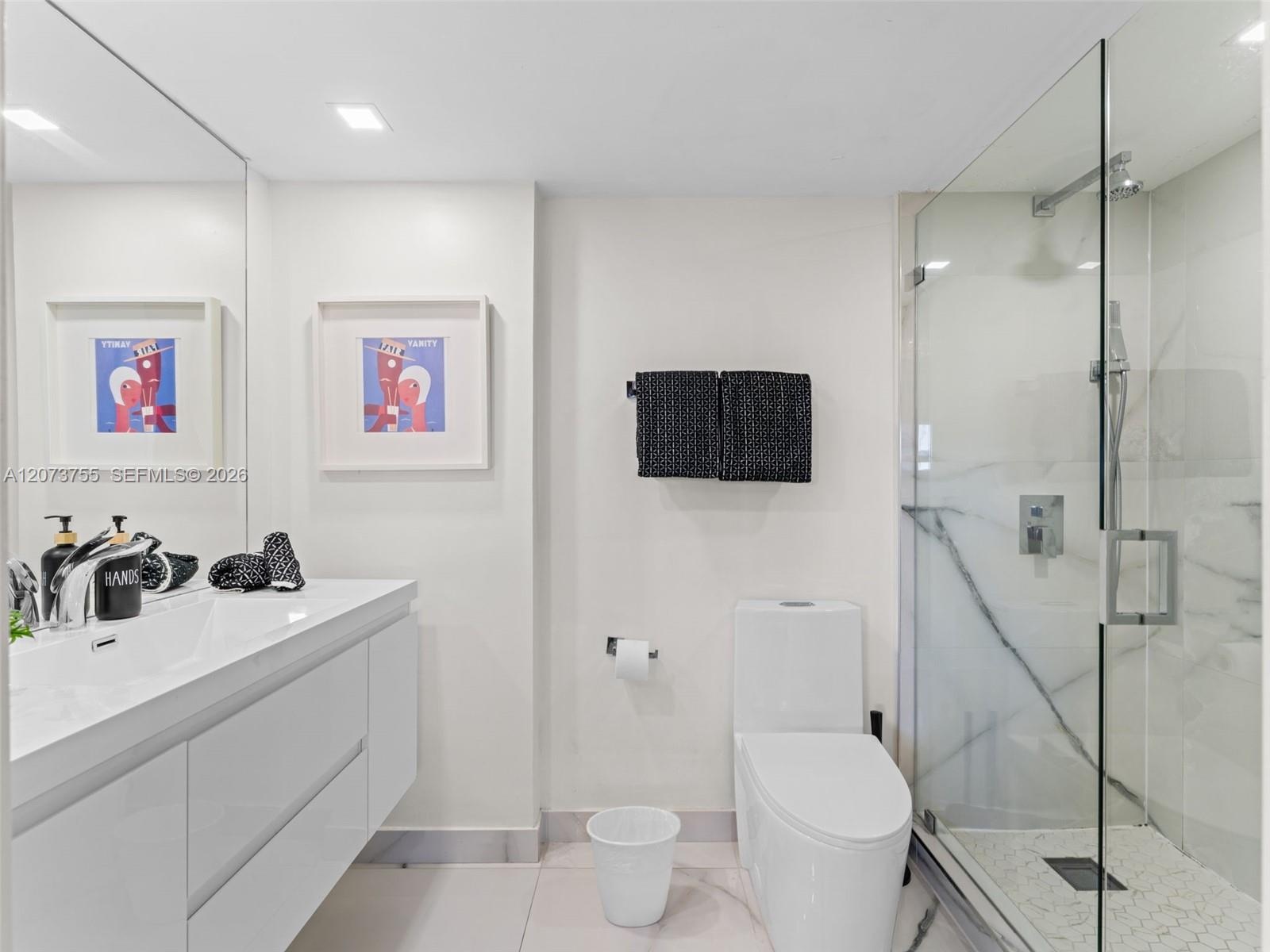 Floating white vanity with integrated sink, glass-enclosed walk-in shower with stone-style wall tile, large frameless wall mirror, and recessed lighti