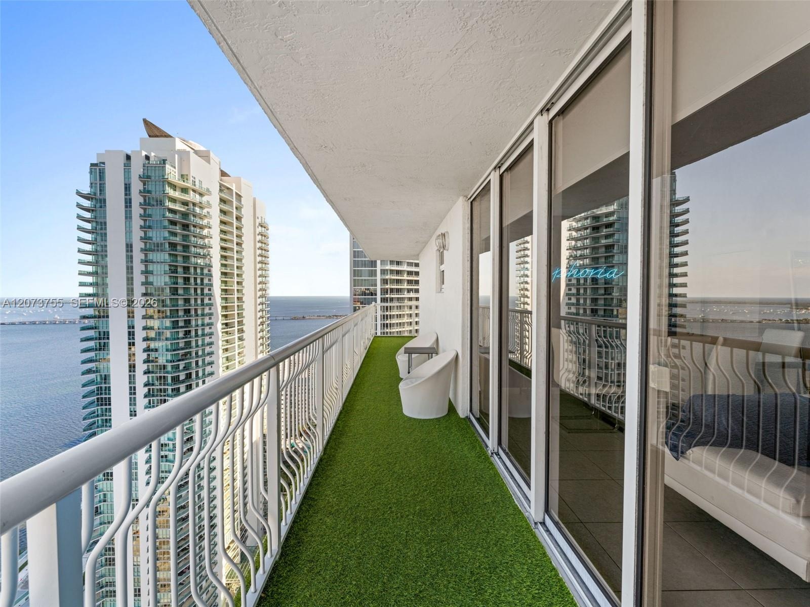 Covered balcony featuring white metal railings, synthetic turf flooring, and sliding glass door access