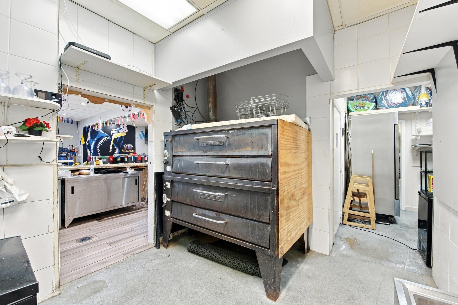 Commercial kitchen featuring a multi-deck industrial oven, stainless steel food preparation surfaces, tiled wall finishes, and recessed ceiling lighti