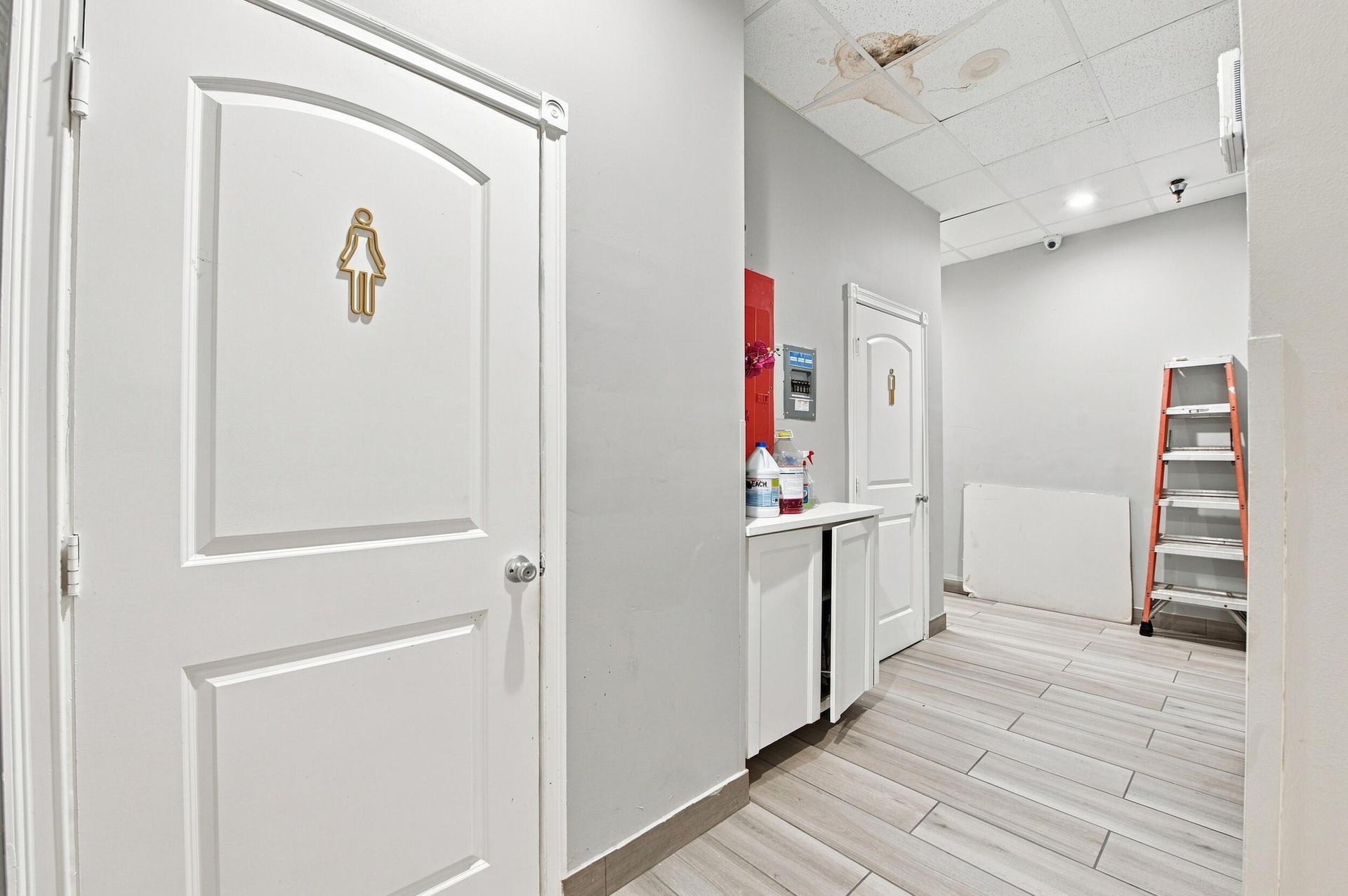 Hallway featuring wood-finish tile flooring, white shaker-style cabinetry, and molded panel doors with metallic hardware