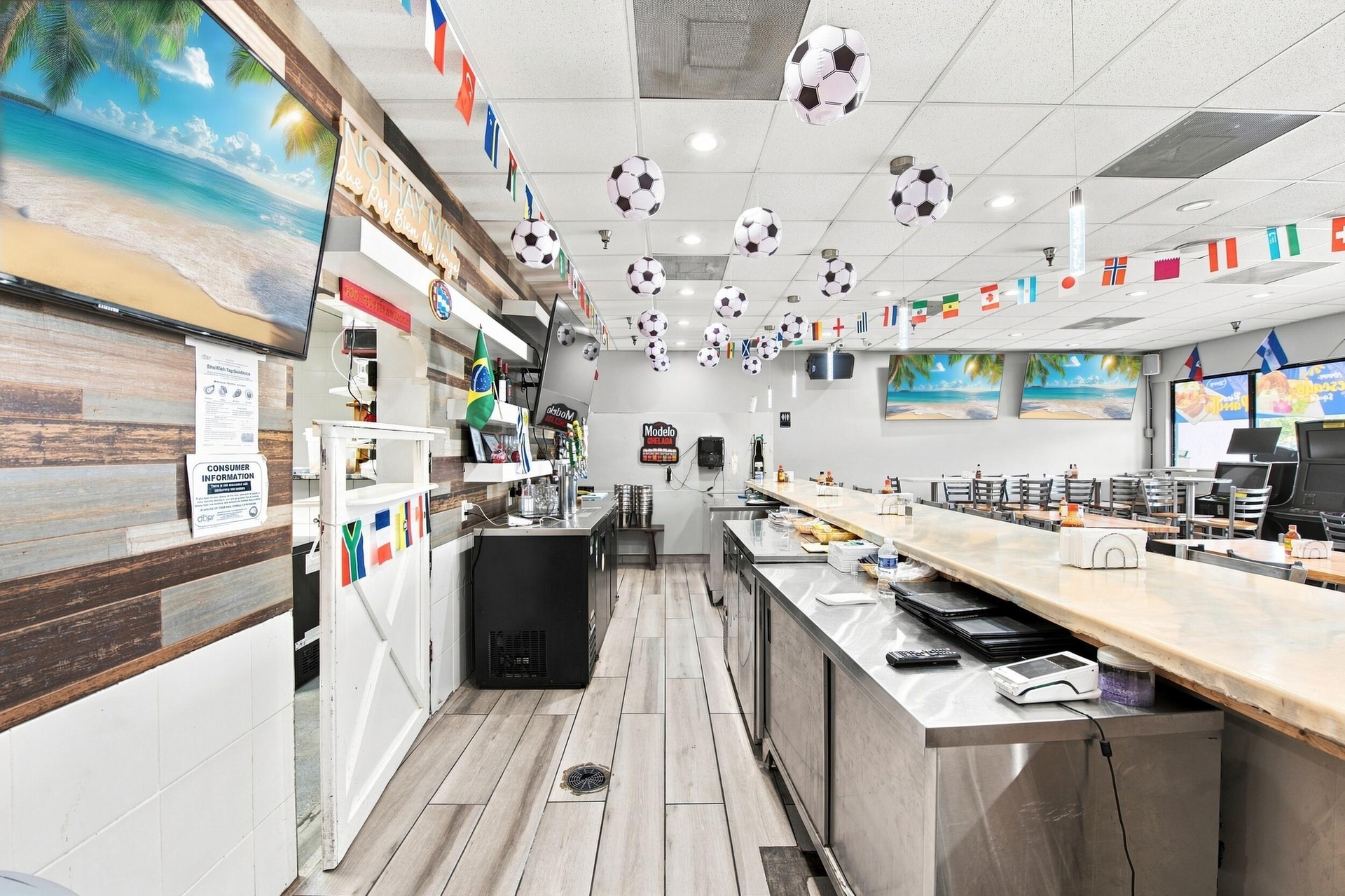 Commercial bar area featuring a long service counter with light-toned surfacing, extensive stainless steel under-counter storage, wood-finish wall pan