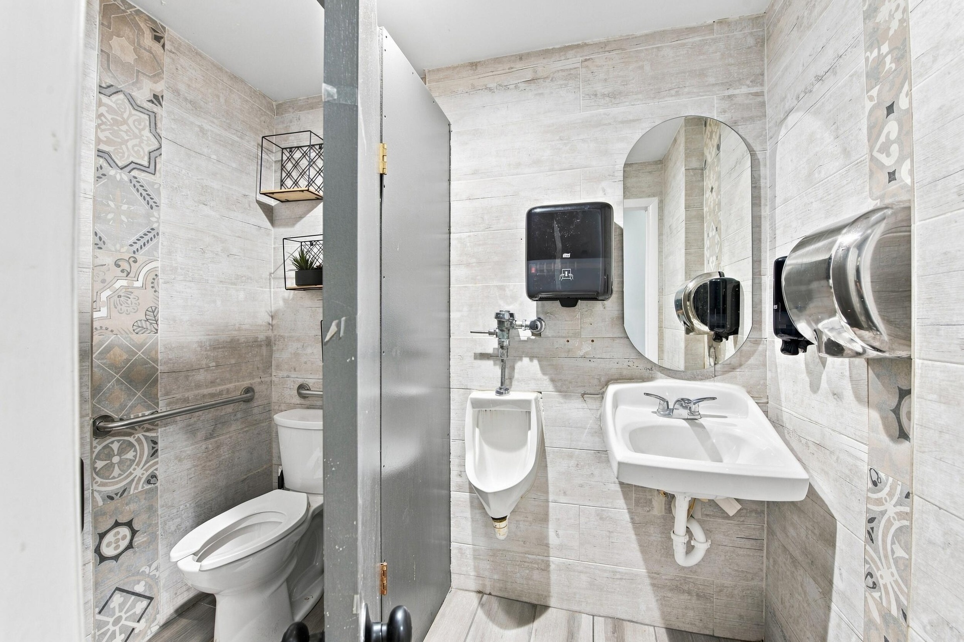 Restroom featuring wood-finish wall tile, patterned decorative tile accents, wall-mounted porcelain sink, wall-mounted urinal, and metal safety grab b