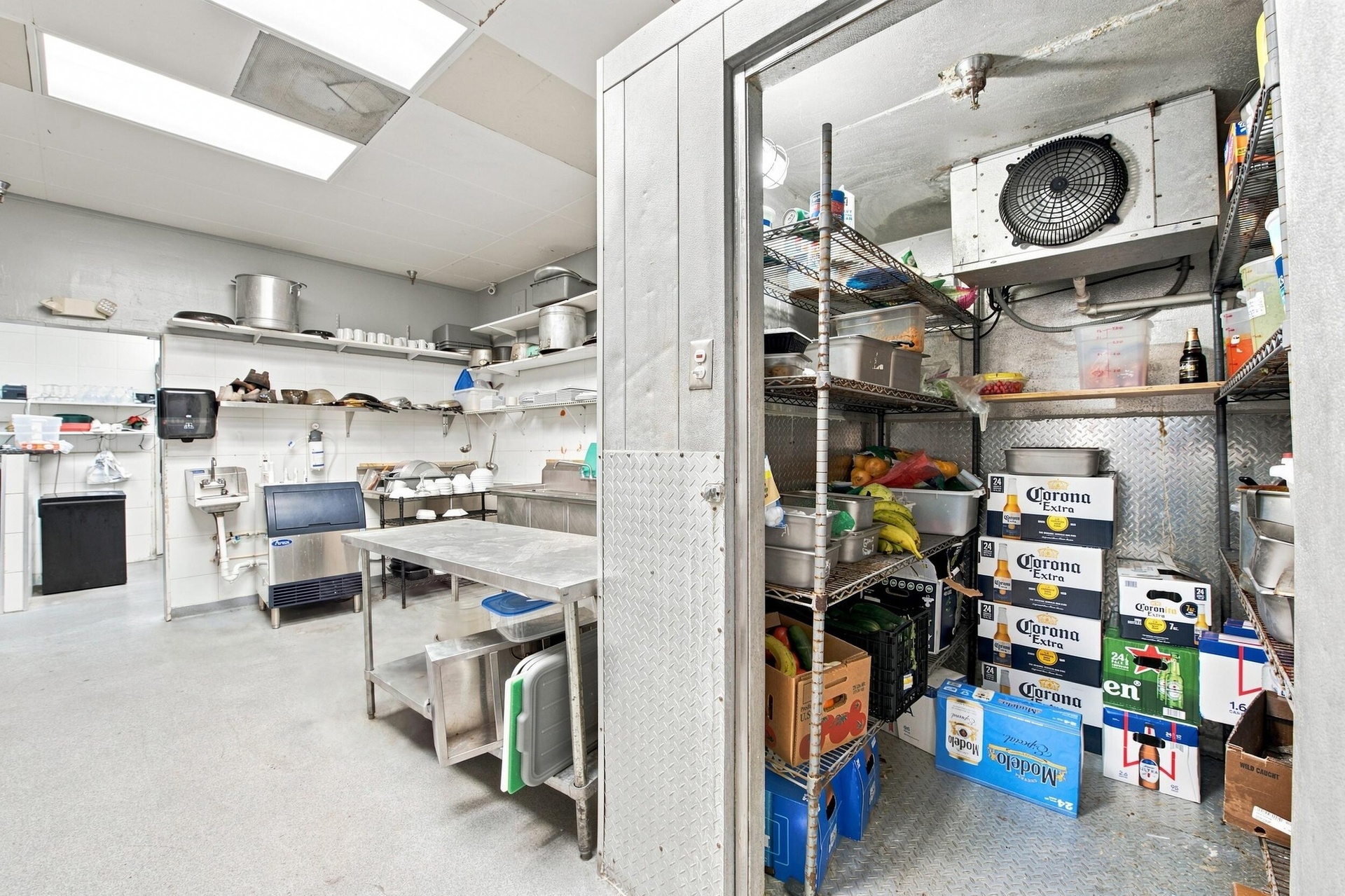Commercial food preparation area featuring a walk-in cooler, stainless steel work table, drop ceiling with recessed lighting, and industrial metal she