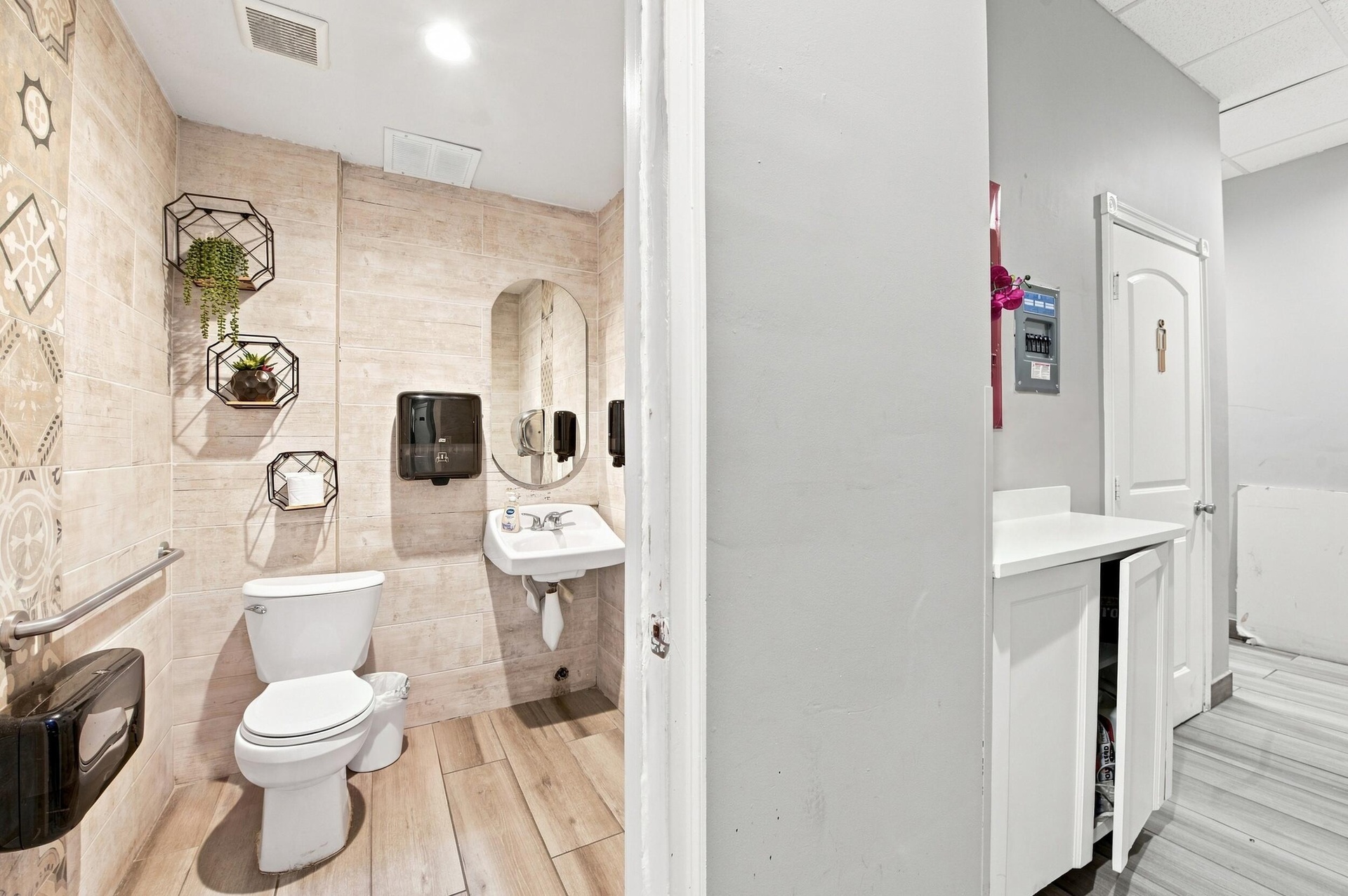 Restroom featuring wood-finish flooring, textured wall tile, wall-mounted sink, oval mirror, and metal grab bar