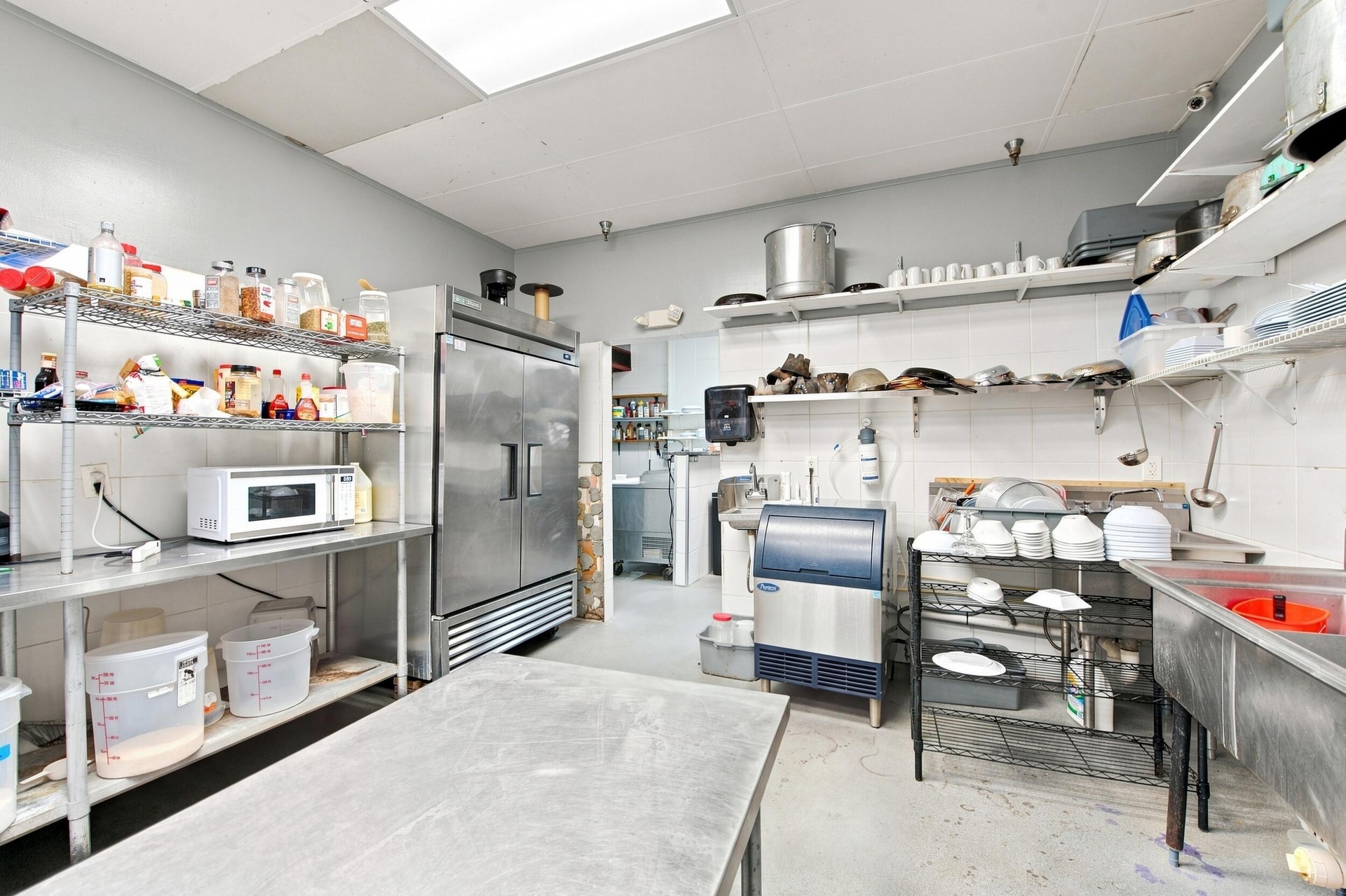 Commercial kitchen prep space featuring stainless steel upright refrigeration, an integrated ice machine, multi-tier wire shelving, and stainless stee