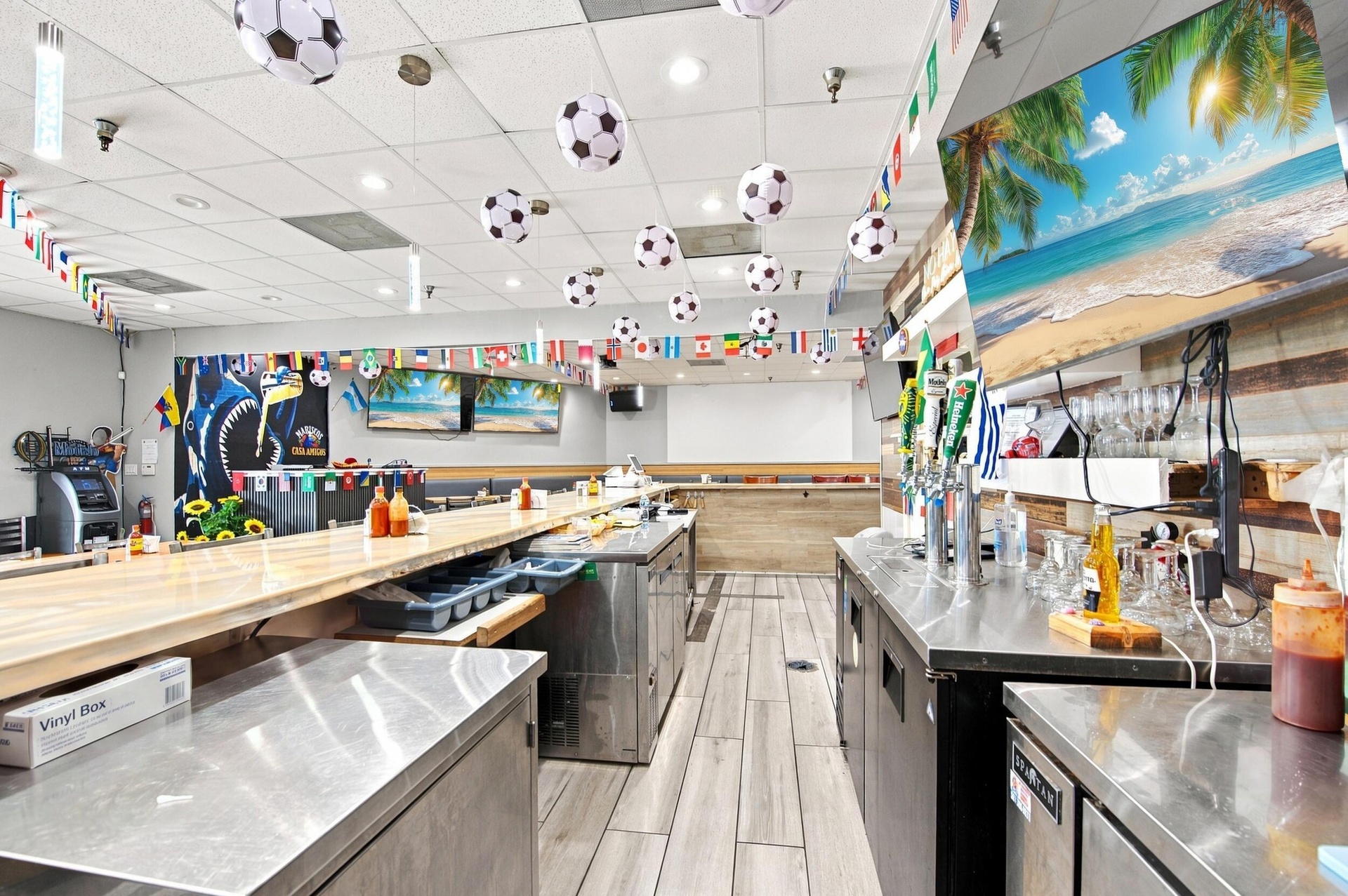 Commercial service area featuring a wooden bar top, stainless steel prep surfaces, multi-tap beverage dispensing system, and wood-finish flooring