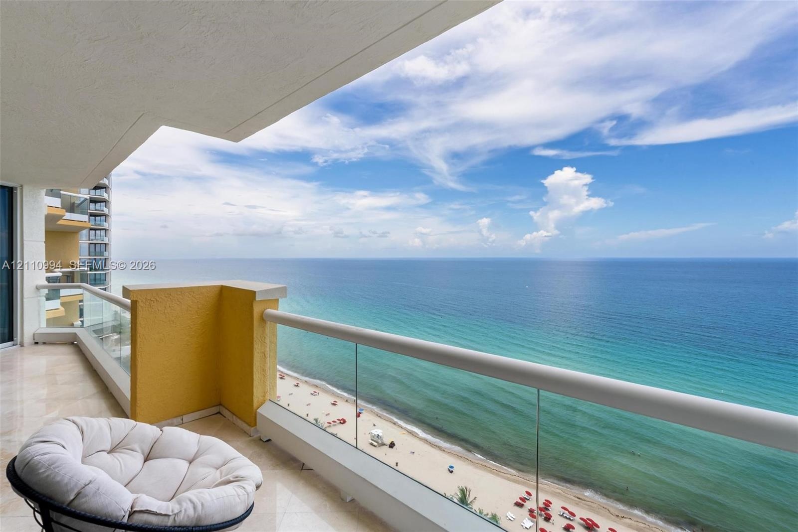 Covered balcony featuring polished stone flooring, glass panel railings, and expansive oceanfront scenery