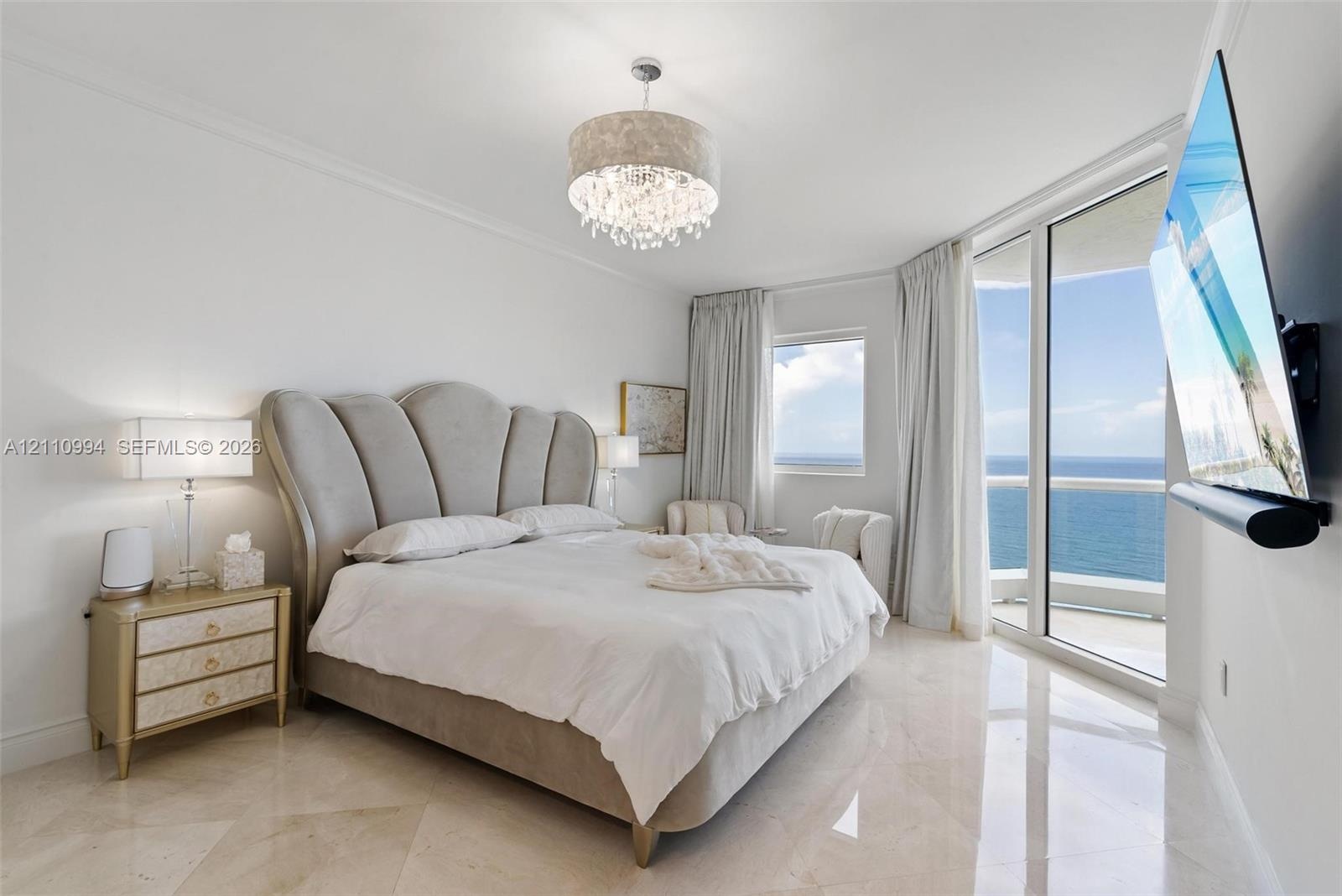 Polished tile flooring, floor-to-ceiling glass paneling, balcony access, and an ornate drum-style chandelier