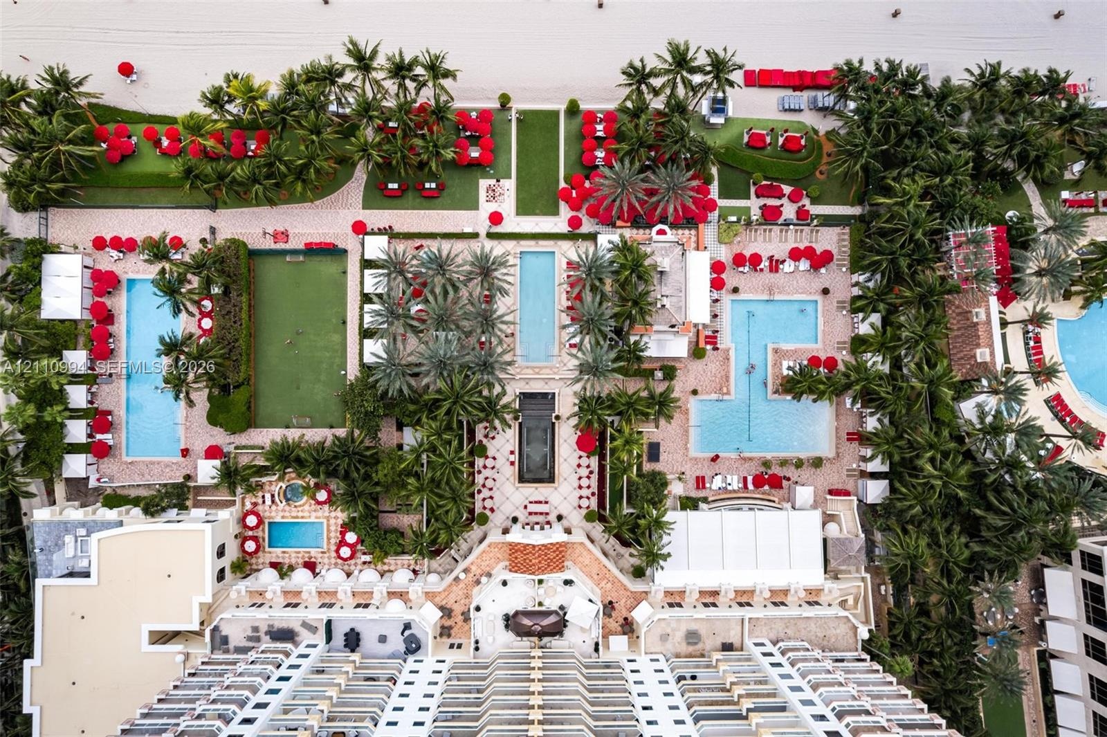 Aerial perspective featuring multi-level swimming pools, manicured palm landscaping, private putting green, and stone-paved courtyards with direct bea
