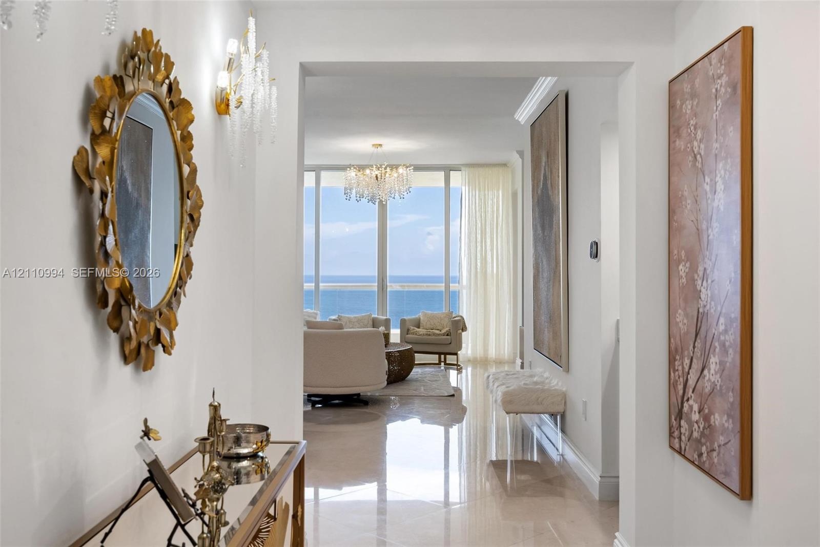 Entryway featuring polished stone-finish flooring, crown molding, and crystal wall-mounted light fixtures, leading to floor-to-ceiling windows with oc