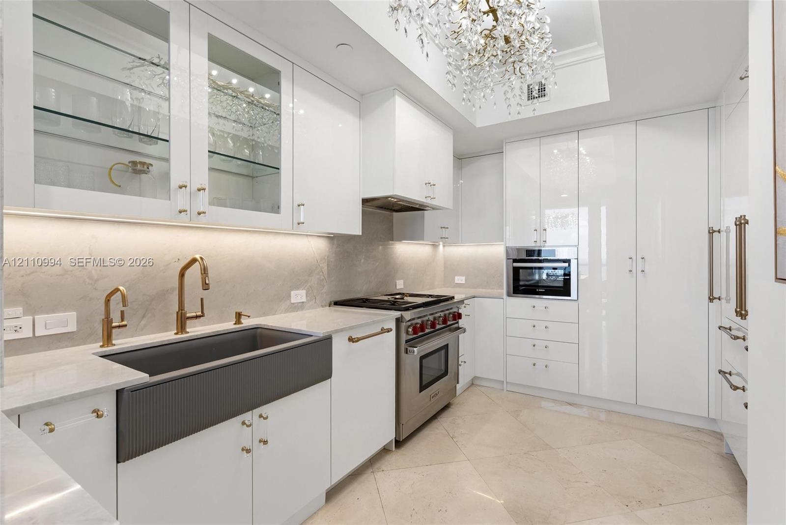 Kitchen featuring high-gloss cabinetry, stone-finish countertops, a dark-toned apron-front sink with gold-tone fixtures, stainless steel professional-