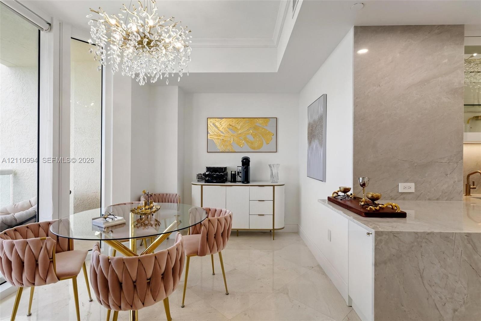 Large-format stone tile flooring, statement crystal chandelier, neutral-tone stone slab countertop, and floor-to-ceiling glass panel door