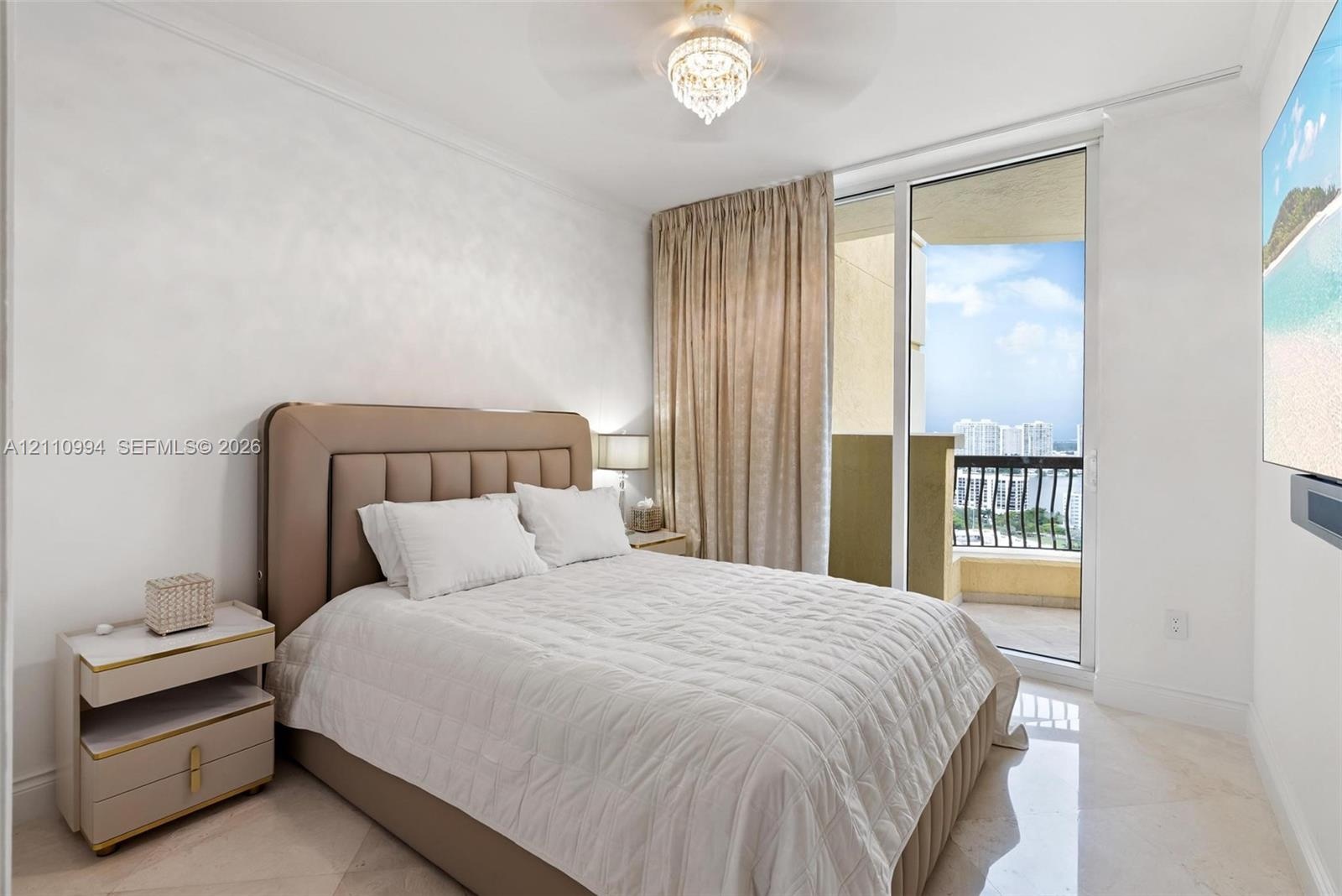 Floor-to-ceiling glass sliding door with access to a balcony, polished stone flooring, and crystal-accented ceiling fan with light fixture