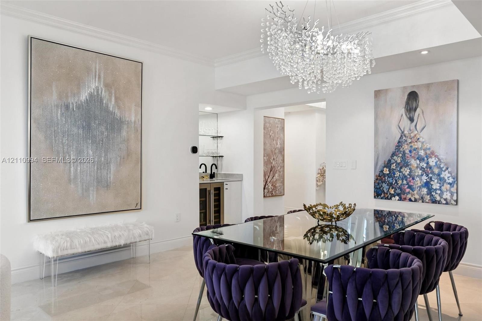 Statement chandelier with crystal accents, polished stone flooring, and a built-in wet bar featuring cabinetry, glass shelving, and a beverage refrige