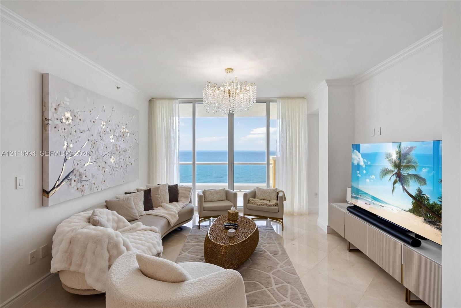 Living space featuring polished stone flooring, crown molding, a crystal chandelier, floor-to-ceiling glass wall, and direct ocean backdrop