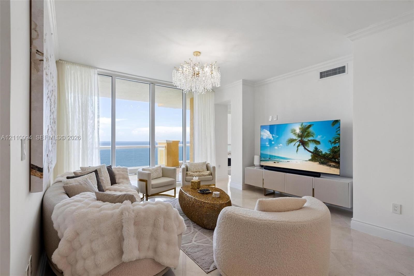 Living space featuring floor-to-ceiling glass panel doors, polished stone flooring, a multi-tiered crystal chandelier, and crown molding