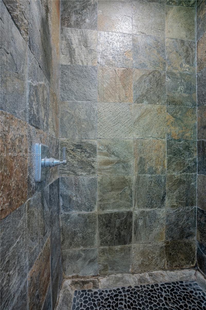 Shower enclosure featuring textured natural stone wall tiles and a polished metal shower control fixture, complemented by a pebble-tiled floor