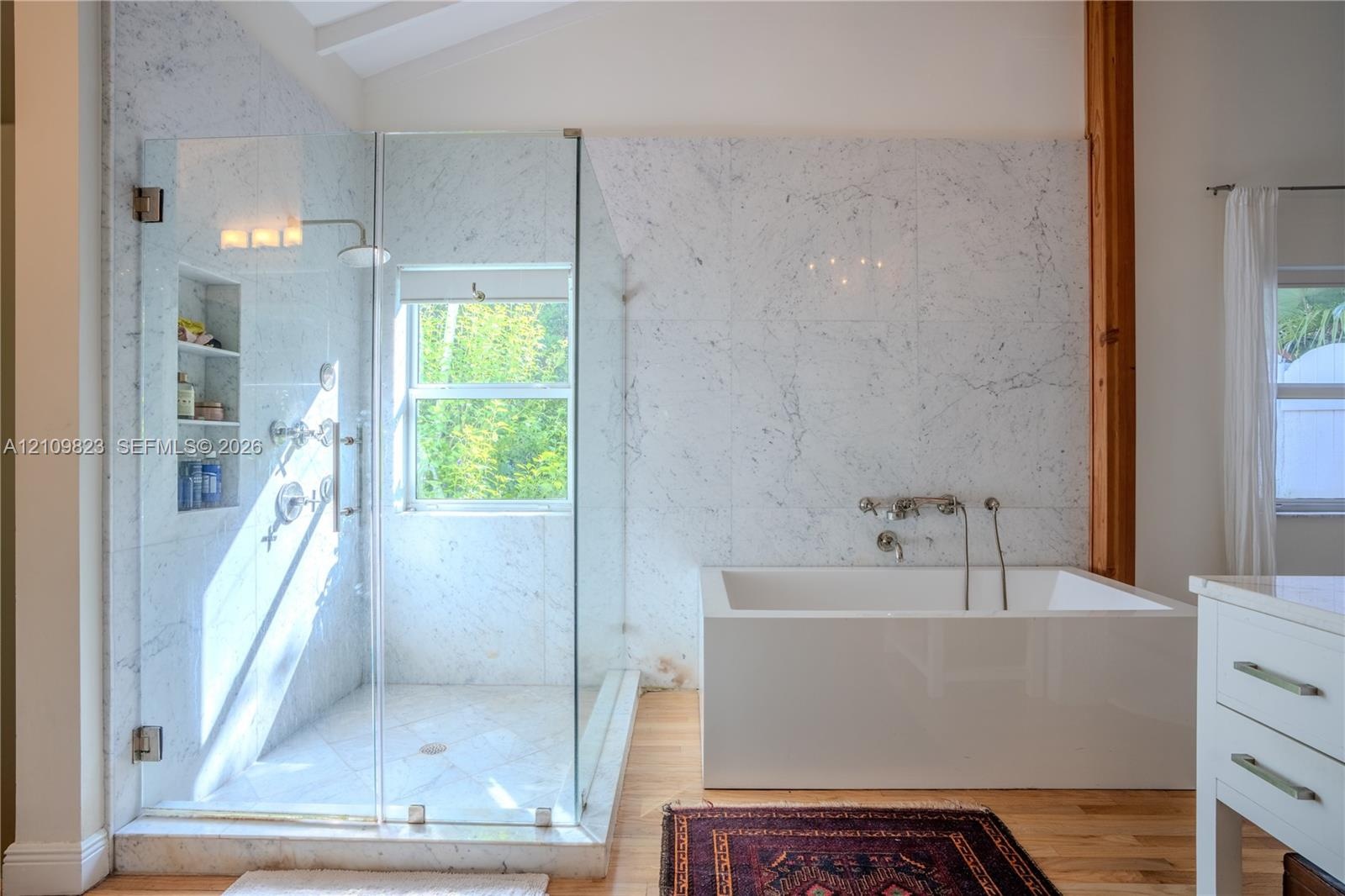 Walk-in shower with frameless glass enclosure, built-in shelving, and large-format stone tiling
