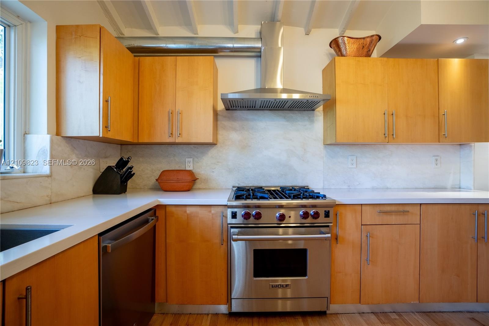 Kitchen featuring flat-panel wood cabinetry, stone slab backsplash, solid surface countertops, stainless steel professional-grade range, and exposed c