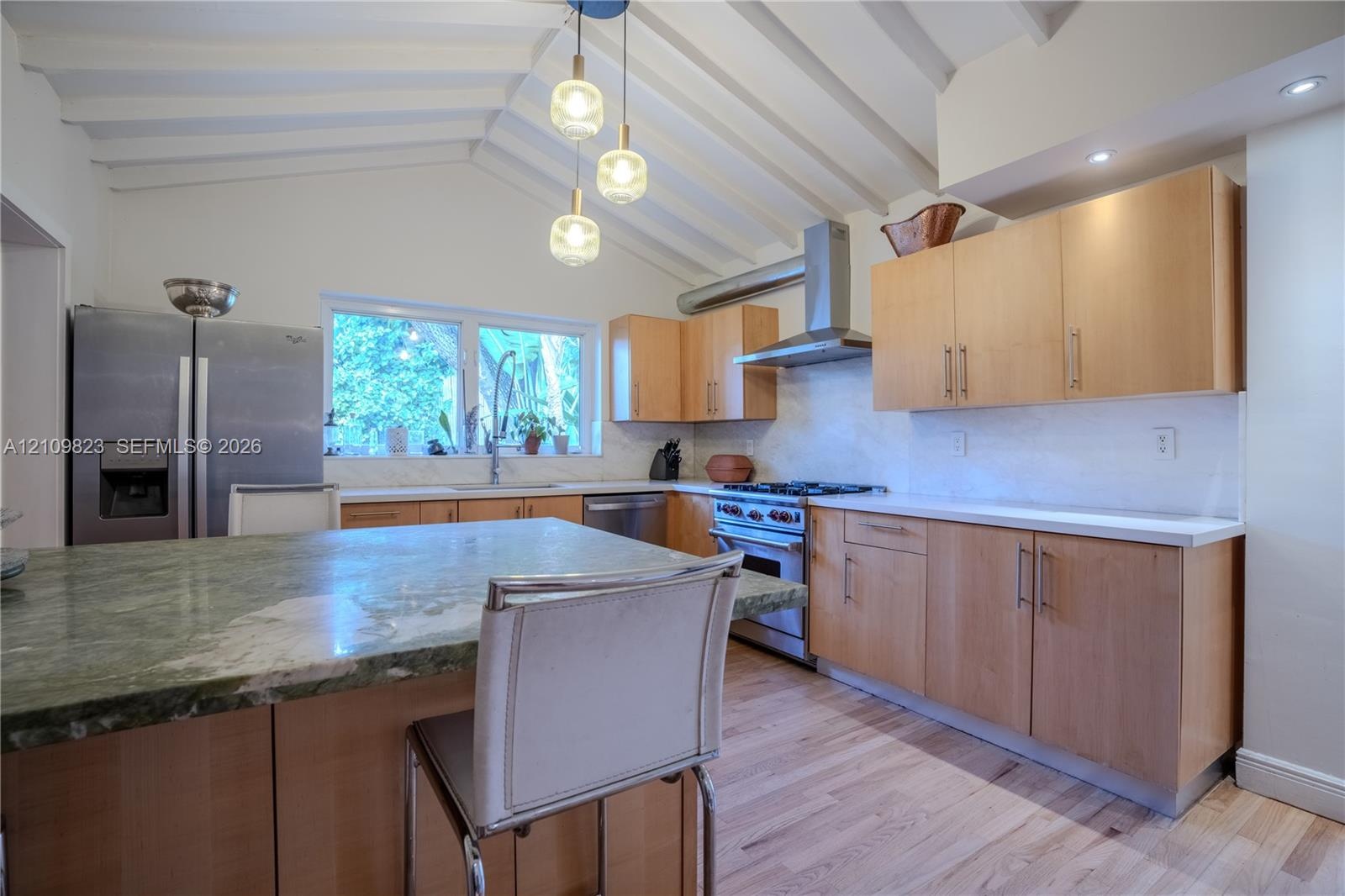 Kitchen featuring a vaulted ceiling with exposed beams, natural wood-finish cabinetry, a stone-surfaced kitchen island, stainless steel appliances, an