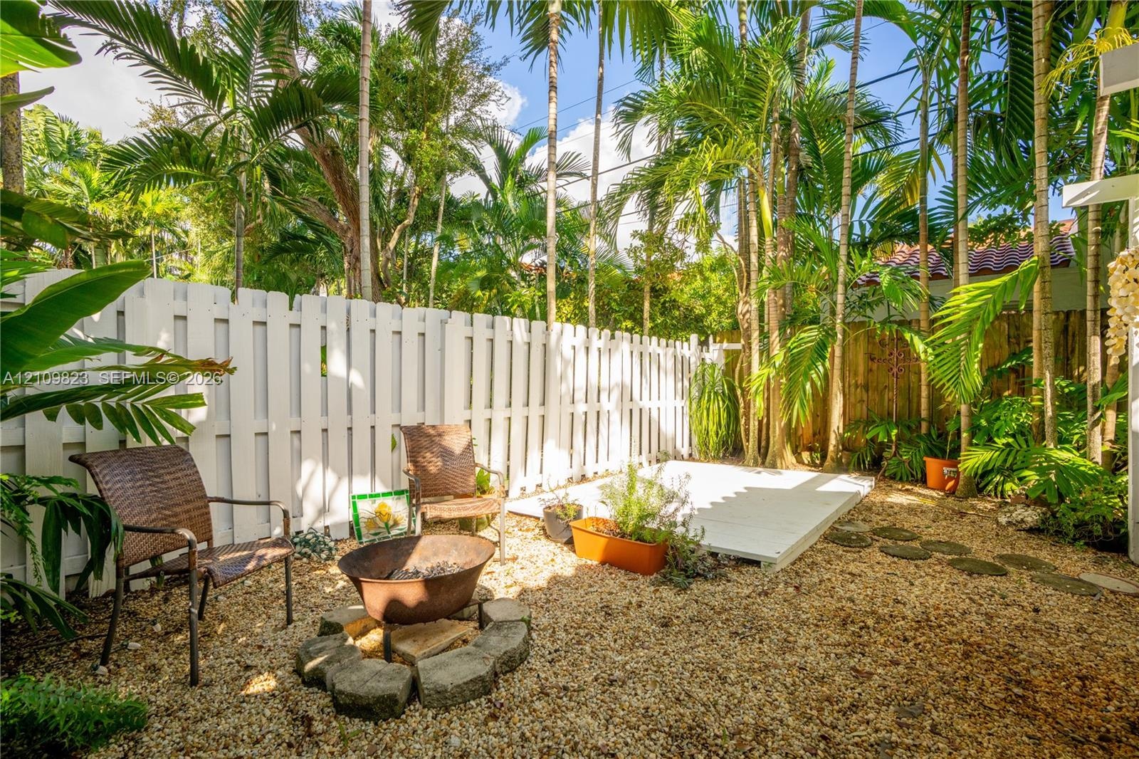 Private backyard featuring a white privacy fence, gravel ground cover, elevated wood deck, and mature palm trees