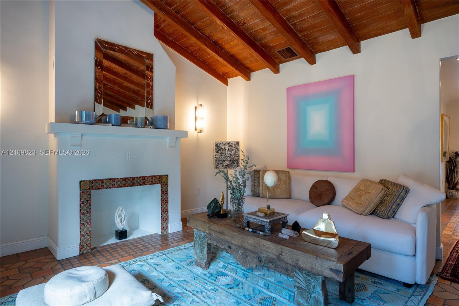 Vaulted ceiling with exposed wood beams, fireplace with decorative tile surround, and terra-cotta tile flooring