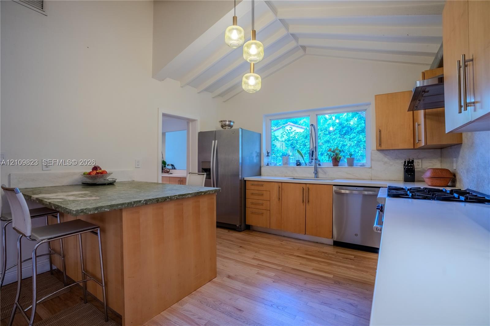 Kitchen featuring vaulted ceilings, wood-finish flooring, a center island with a stone-surface countertop, stainless steel appliances, and multi-light