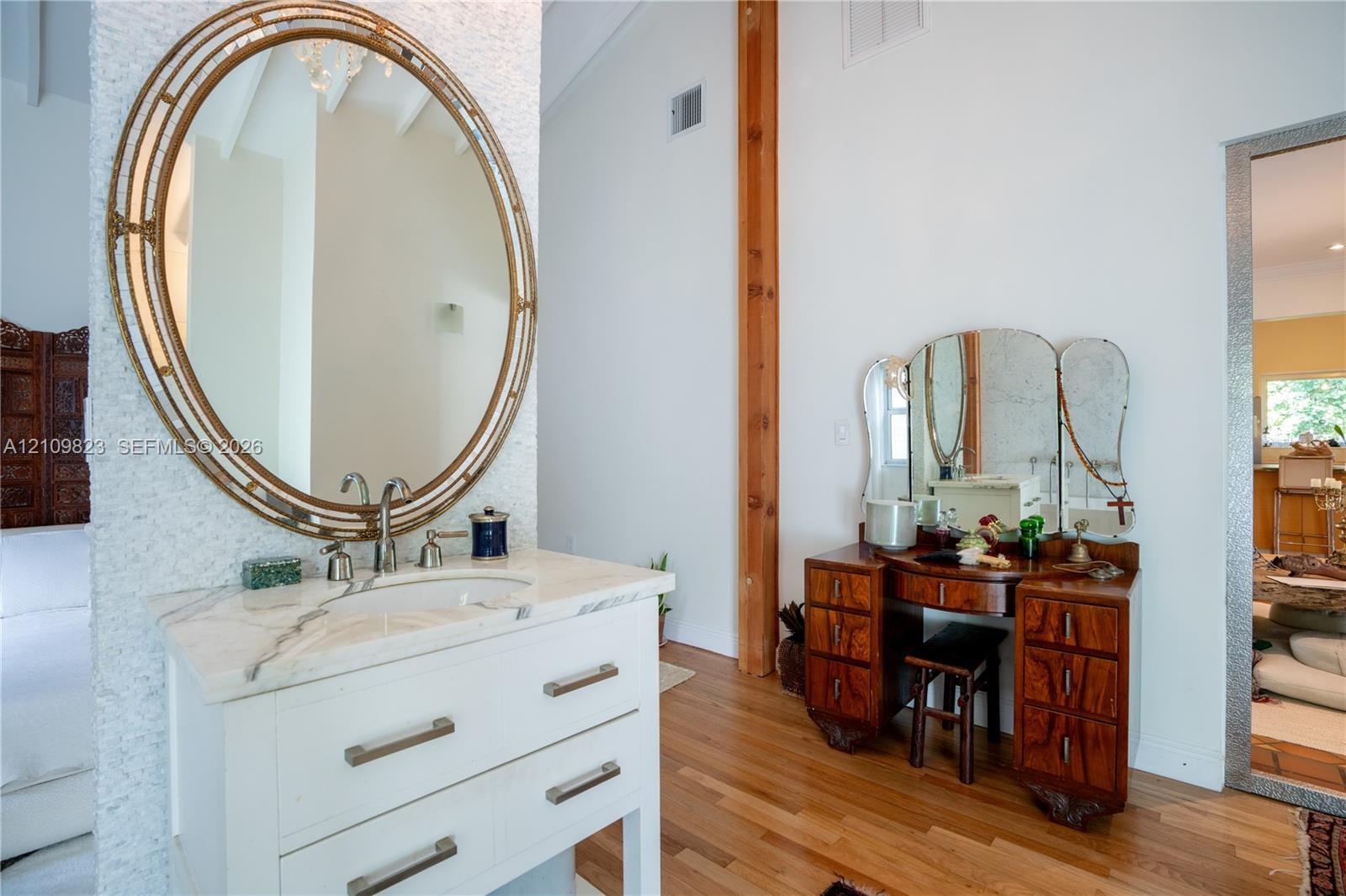 White vanity featuring an integrated basin, stone countertop, and polished hardware, complemented by a large oval mirror with an ornate metal frame, s