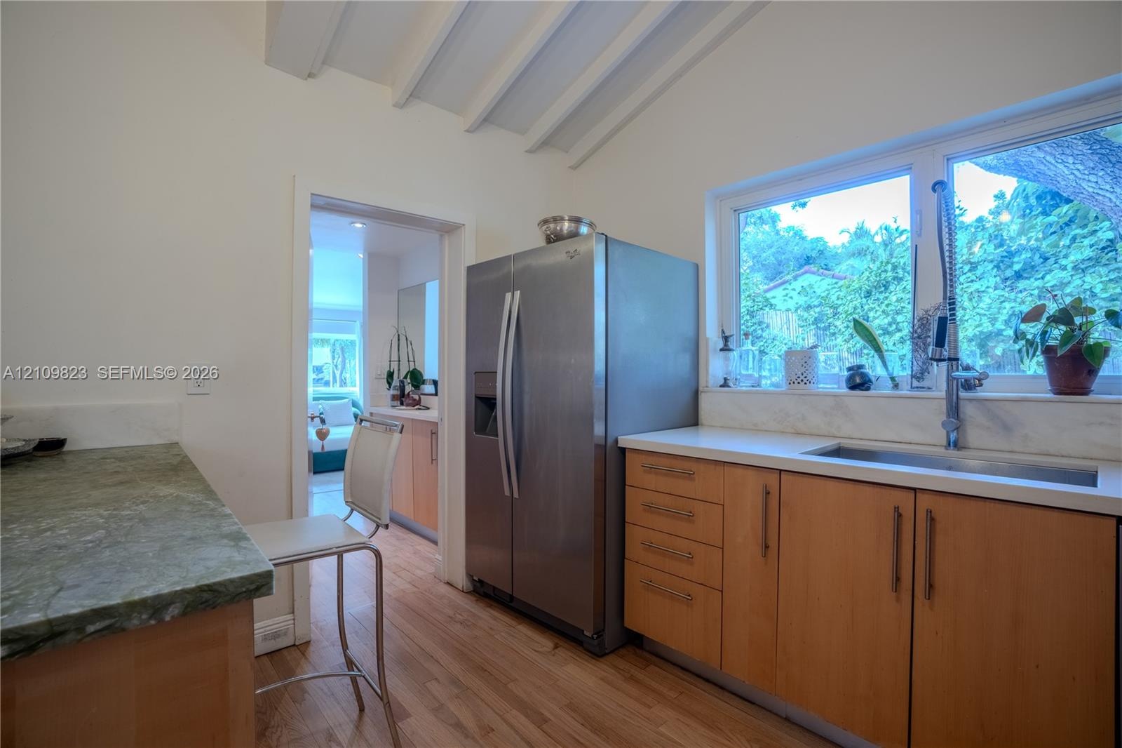 Kitchen featuring wood-finish cabinetry, stone countertops, stainless steel refrigerator, undermount sink with a gooseneck faucet, and exposed beam ce