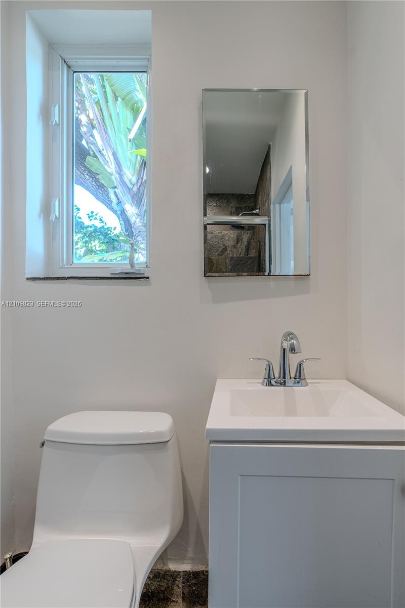 White vanity with a solid-surface countertop and a polished chrome faucet, paired with a frameless rectangular wall mirror, a ceramic toilet, and a wi