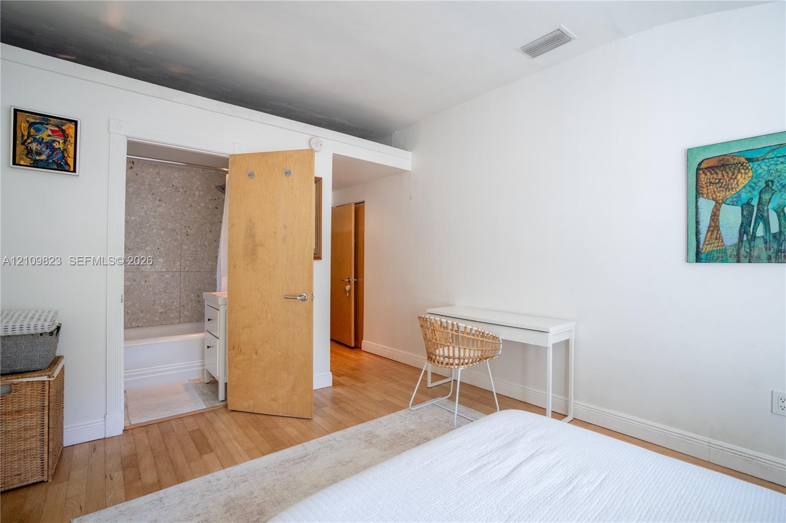 Wood-finish flooring, light wood interior door, and bathroom featuring a tub-shower combination with textured wall tiling