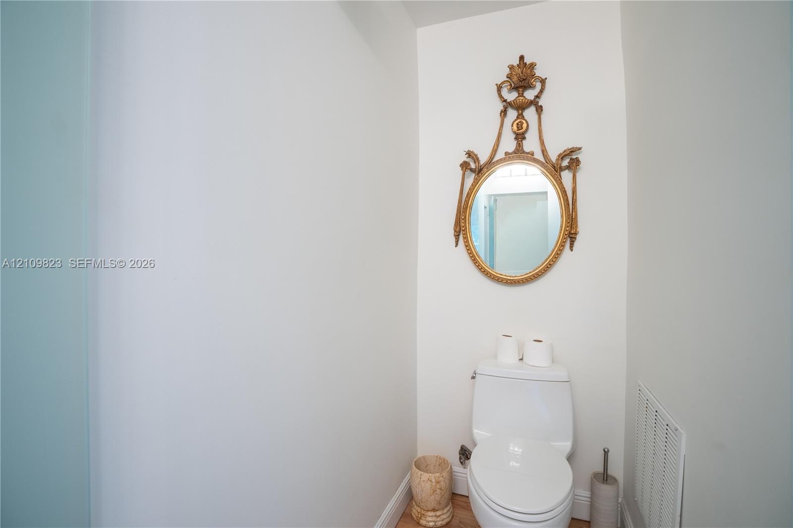 Wall-mounted decorative gold-tone oval mirror featuring ornate detailing and a white high-profile toilet