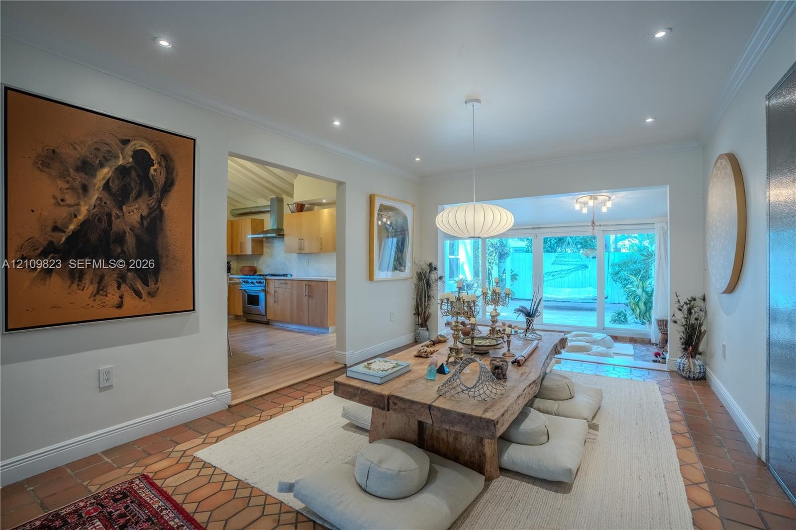 Open-concept interior featuring terracotta tile flooring, recessed lighting, a modern spherical pendant fixture, and large-format glass sliding doors