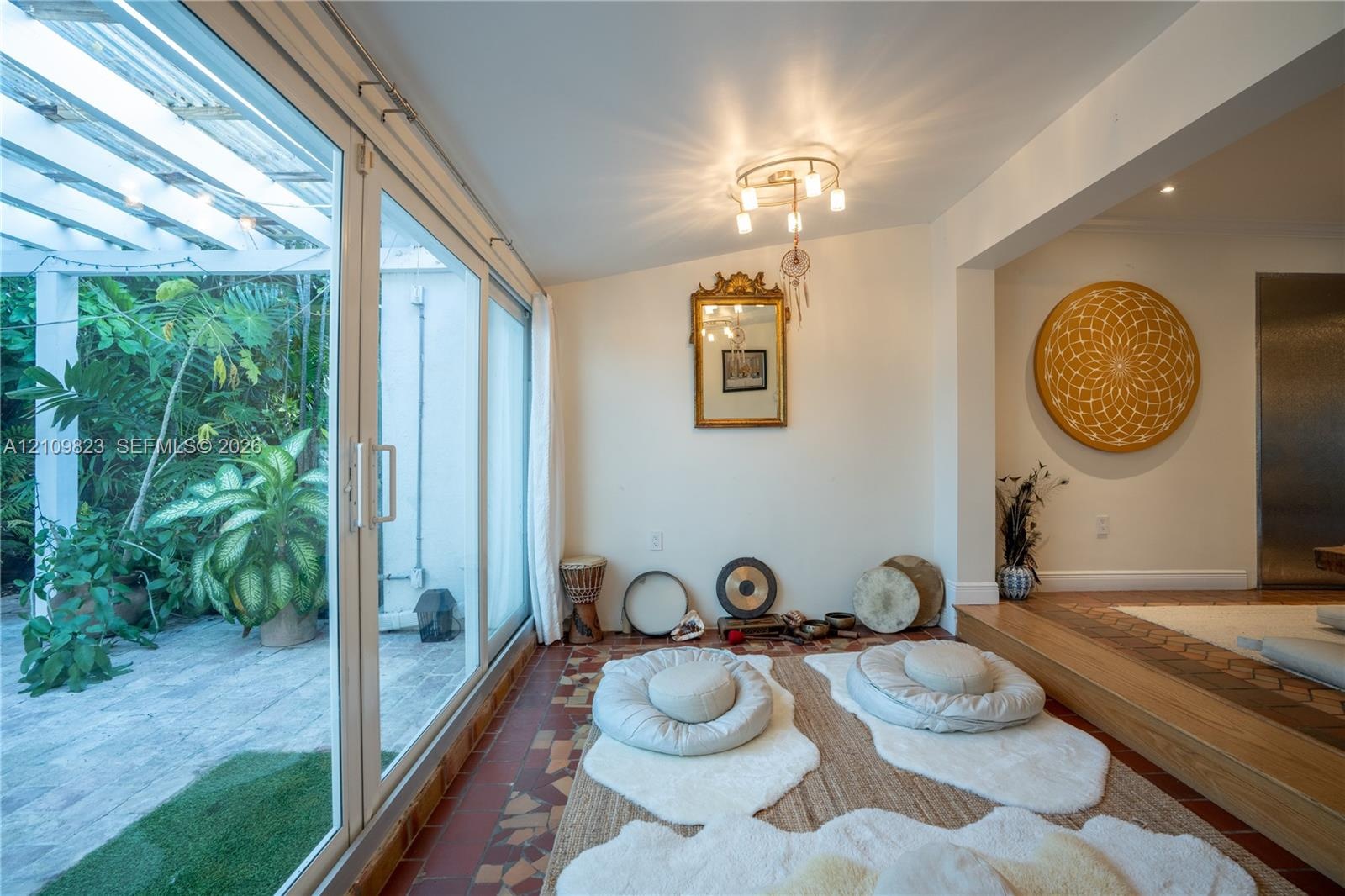 Multi-panel sliding glass doors, overhead pergola structure, terracotta tile flooring, recessed lighting, and raised wood-finish platform